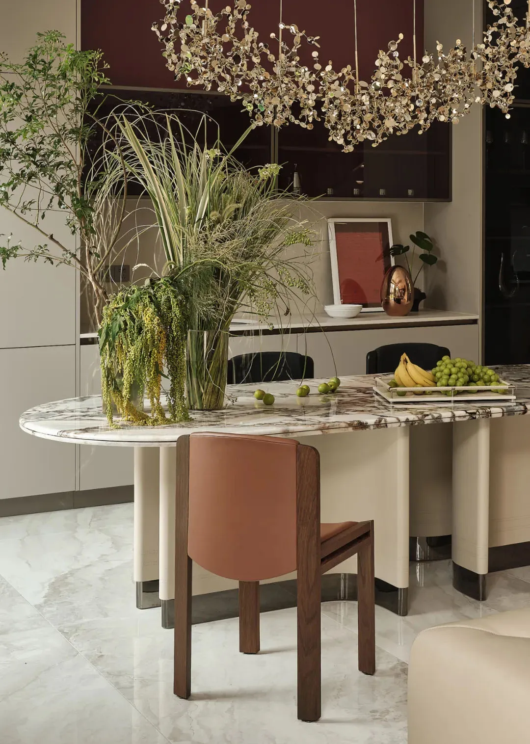 A modern kitchen with a white marble backsplash, featuring a variety of green plants, and a contemporary table with fruit.