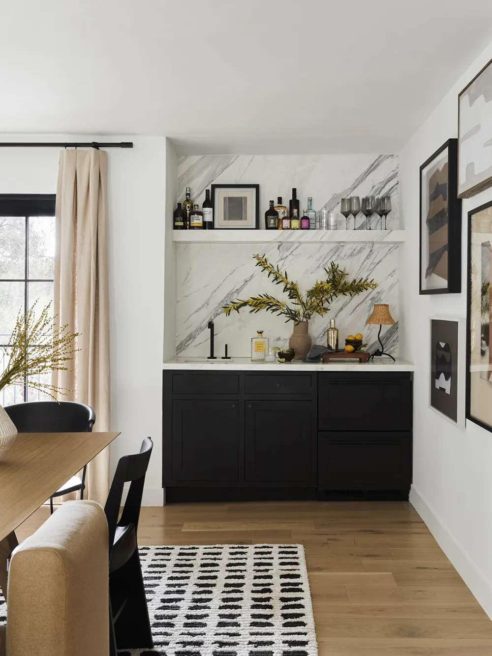 Modern kitchen with black cabinets, marble backsplash, and hardwood floors.