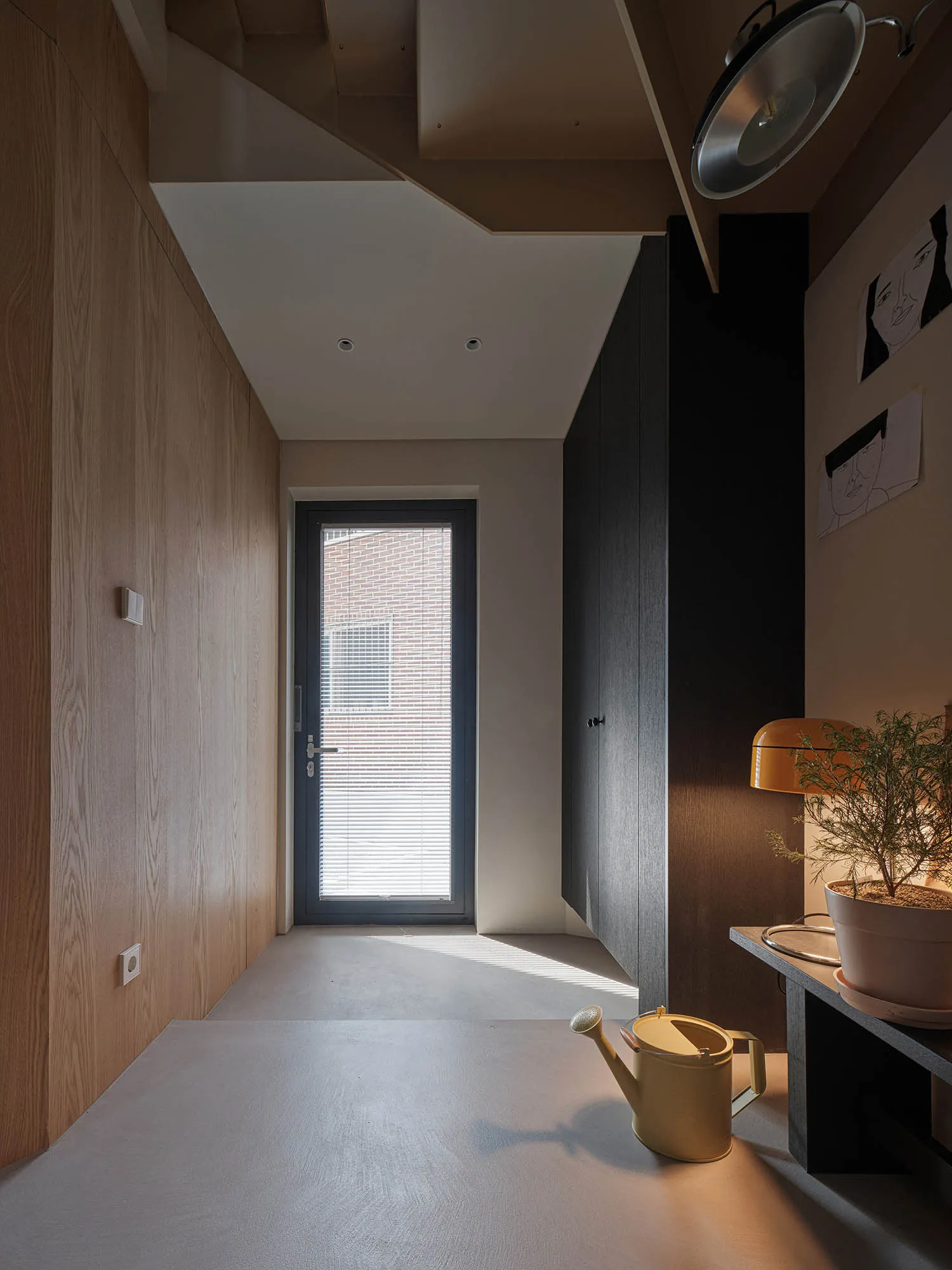 A modern minimalist entryway featuring a concrete floor, minimal decor, and a window with blinds allowing natural light to fi