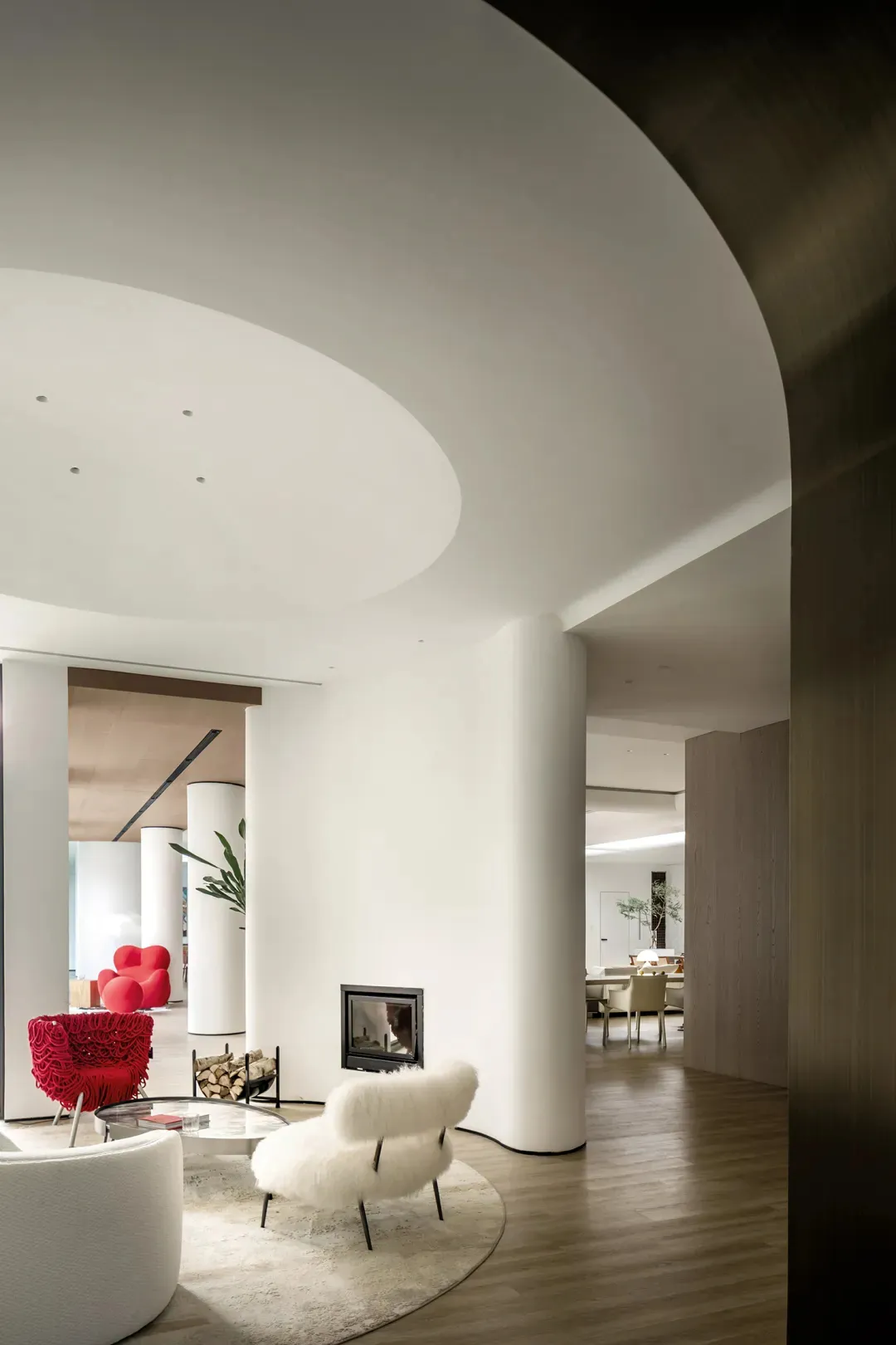 A modern living room with a white fur-covered chair, a round glass table, and a fireplace. The space features clean lines, mi