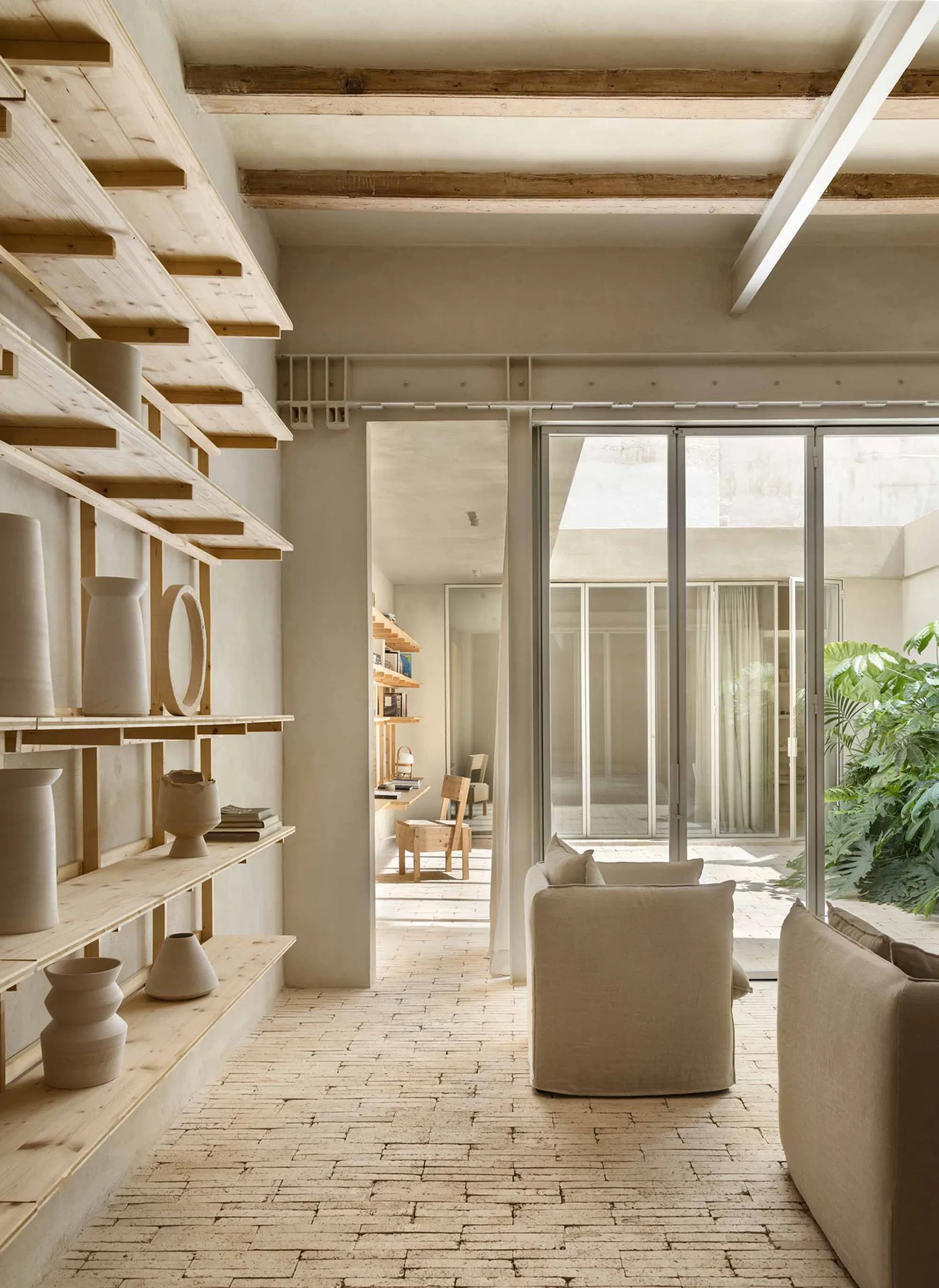 A minimalist living room with concrete walls, wooden furniture, and glass partitions.
