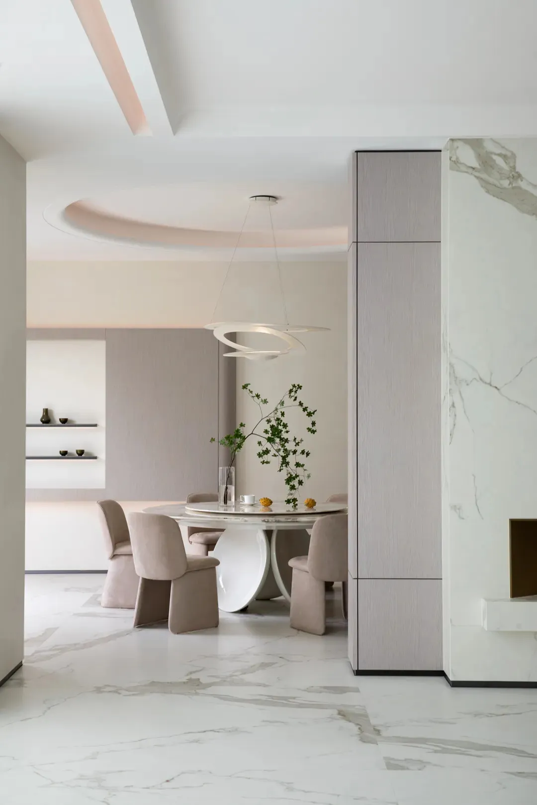 A minimalist dining room featuring a round marble table with a modern light fixture and beige upholstered chairs. Decorative