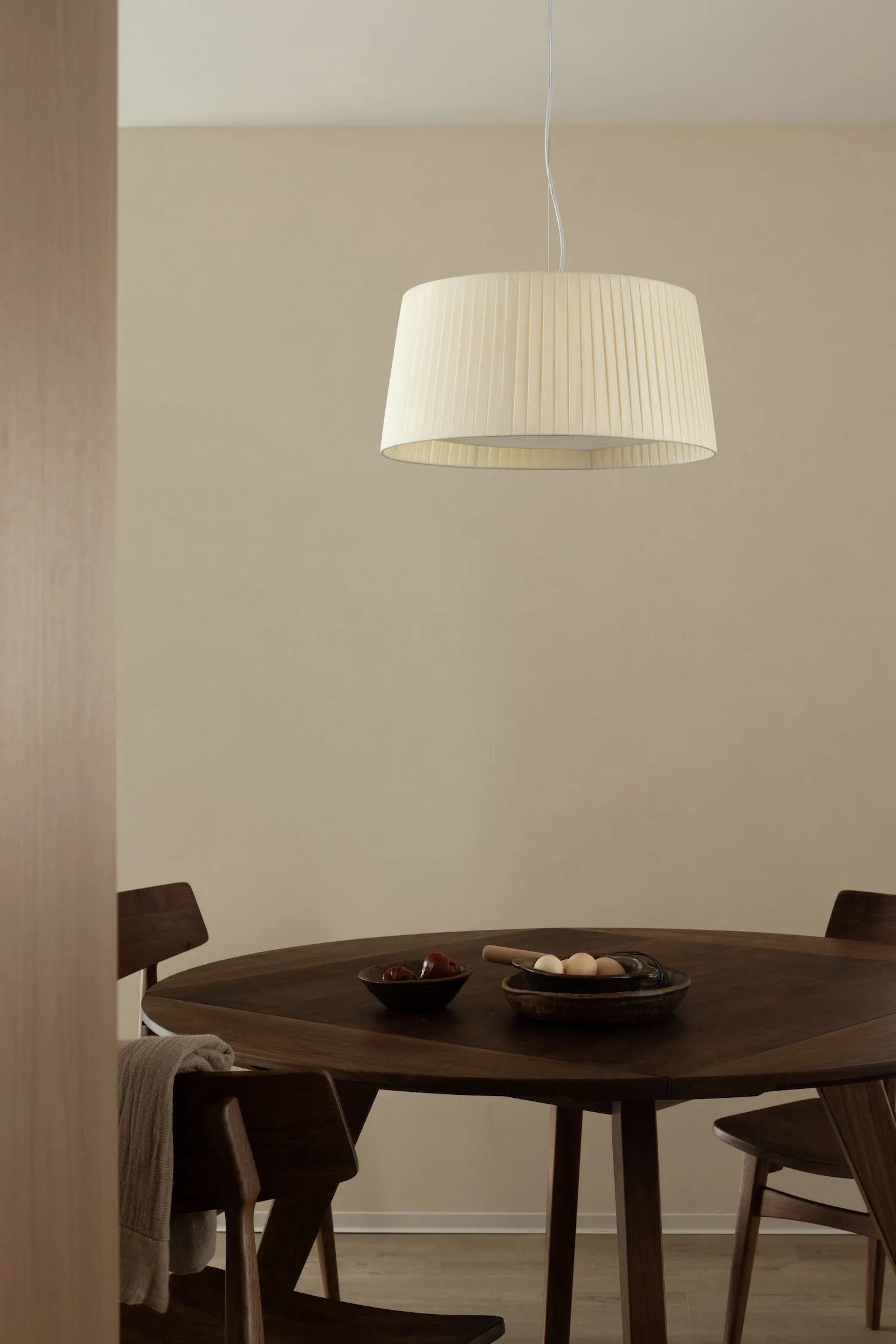 Modern dining room with wooden table and chairs under a pleated light fixture.