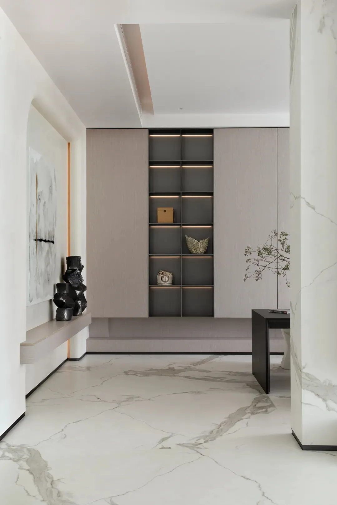 Modern entrance hall designed with marble flooring and walls, featuring a minimalist bookshelf and a contemporary table.