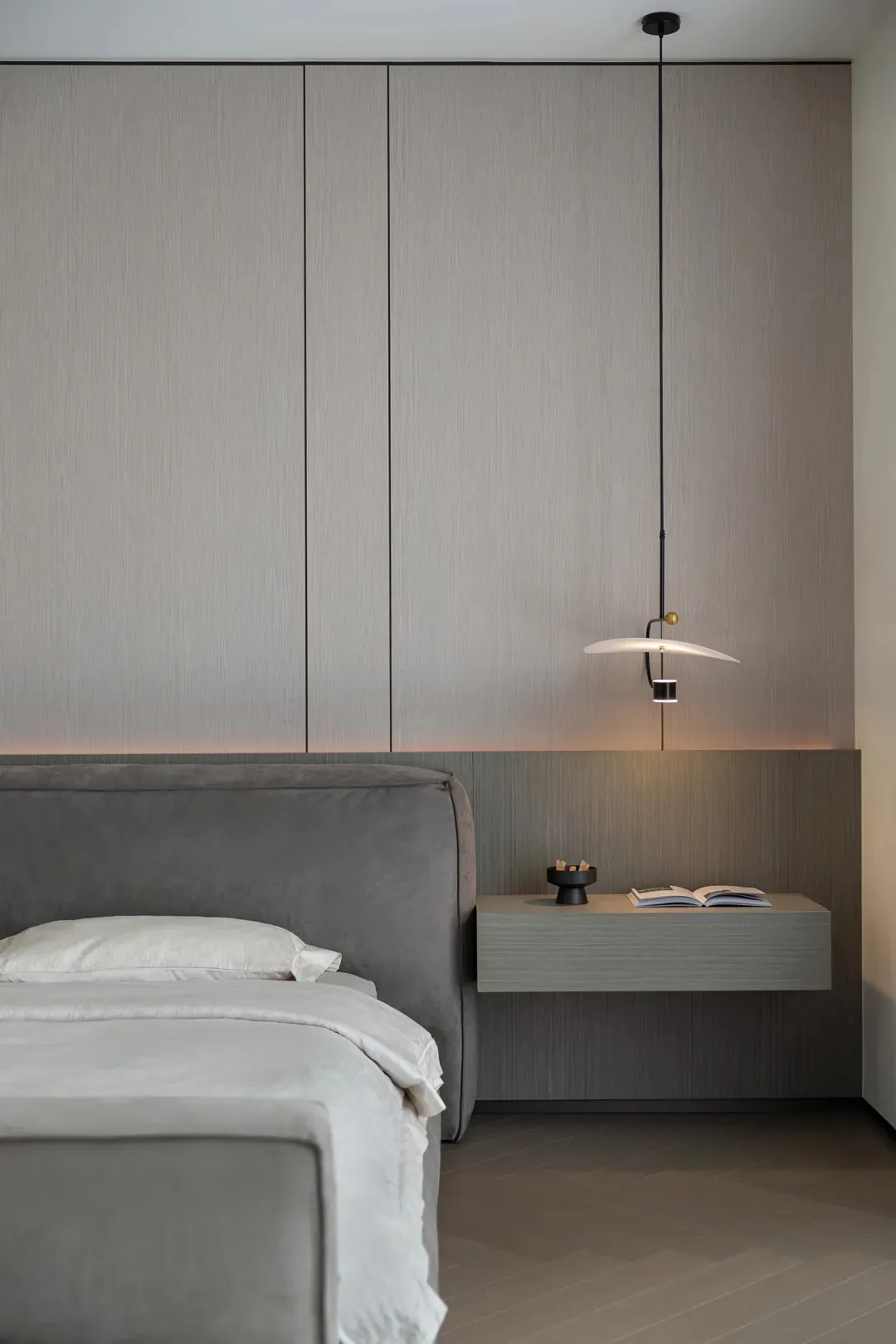 A minimalist bedroom with a neutral color palette, featuring a grey upholstered bed and a floating nightstand with a hanging 