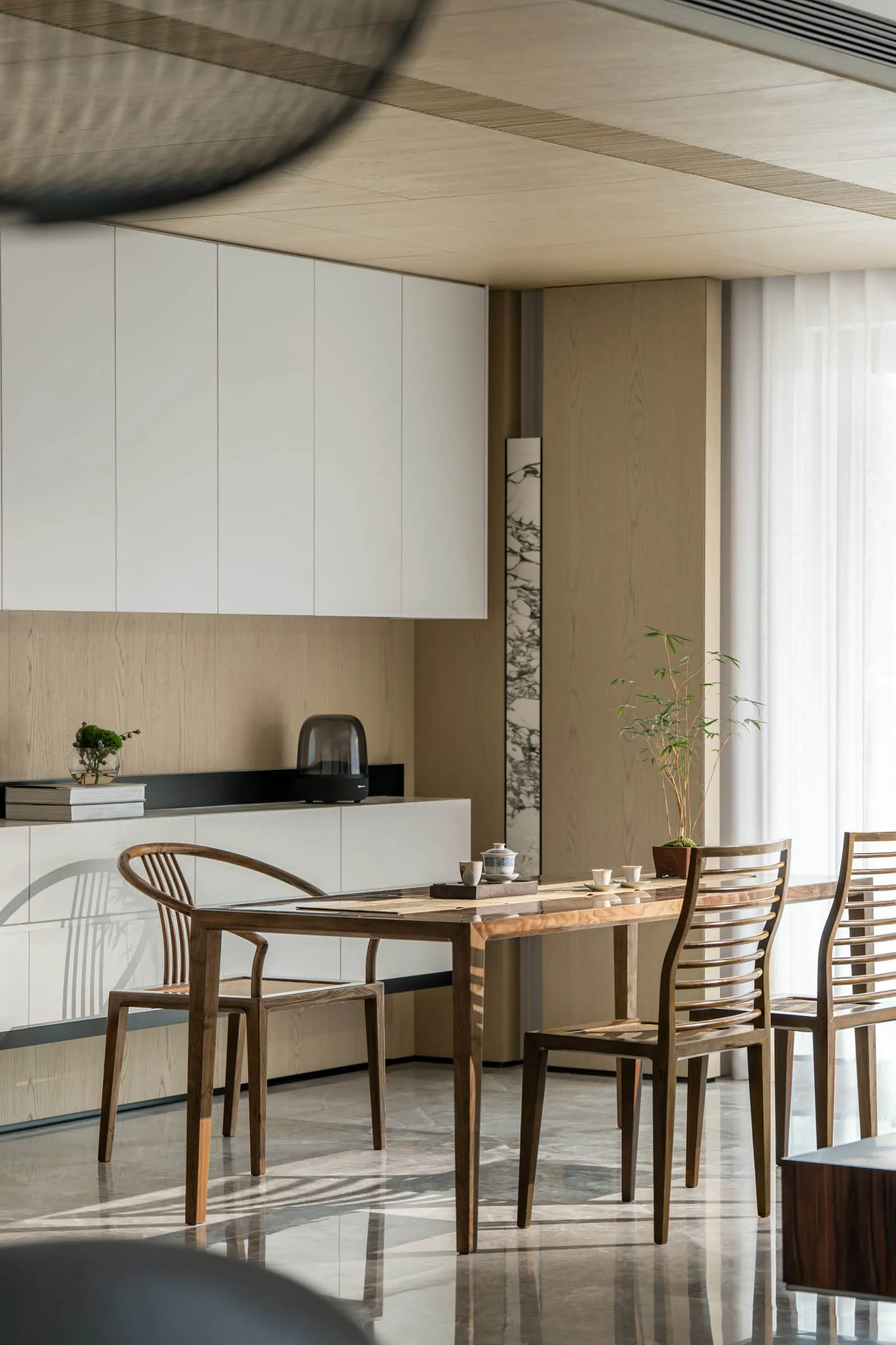 Modern minimalist dining area with wooden chairs and marble dining table, featuring white cabinets and natural light.