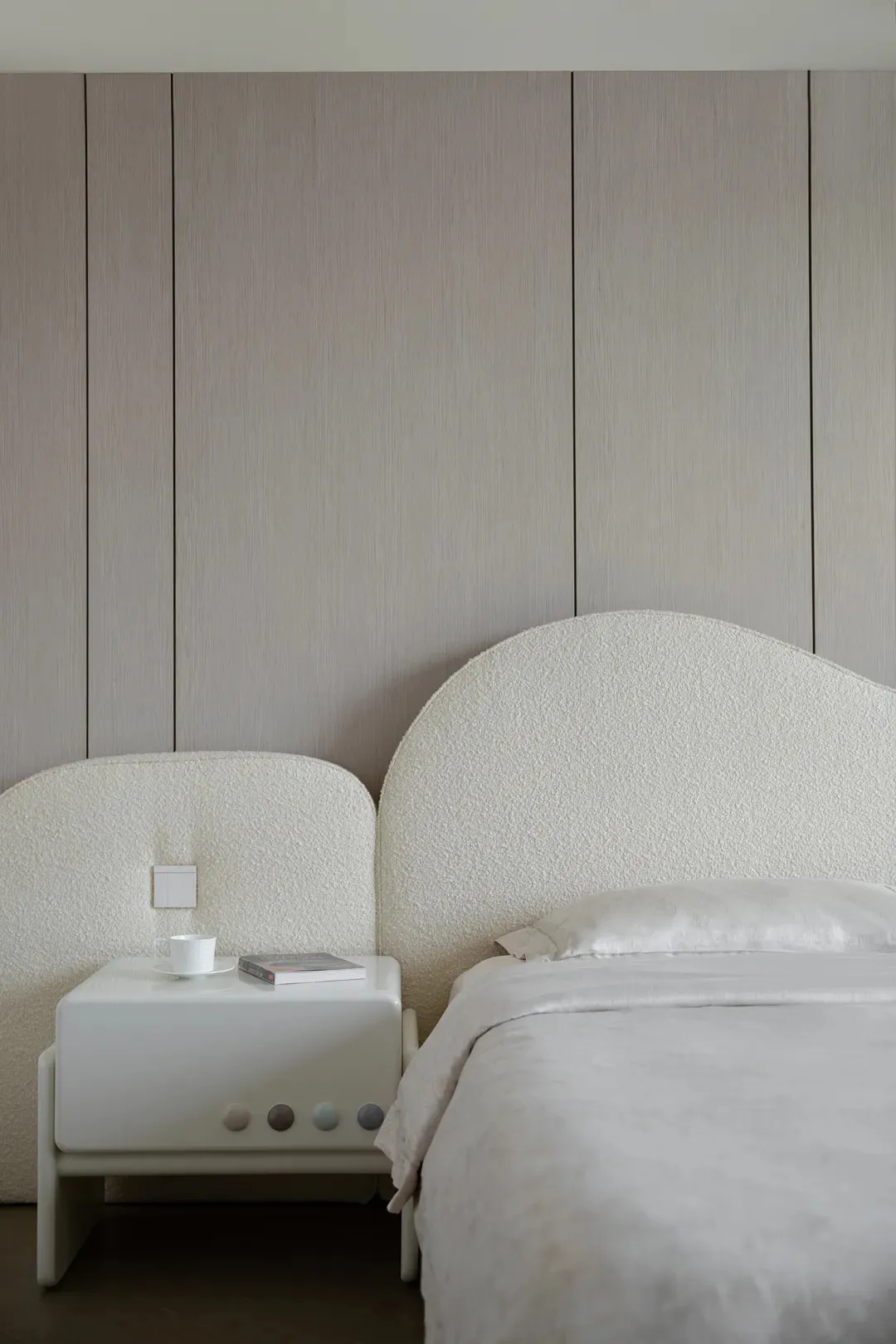 Minimalist bedroom featuring a bed with beige textured fabric headboard and bed frame, against a textured beige wall, with a
