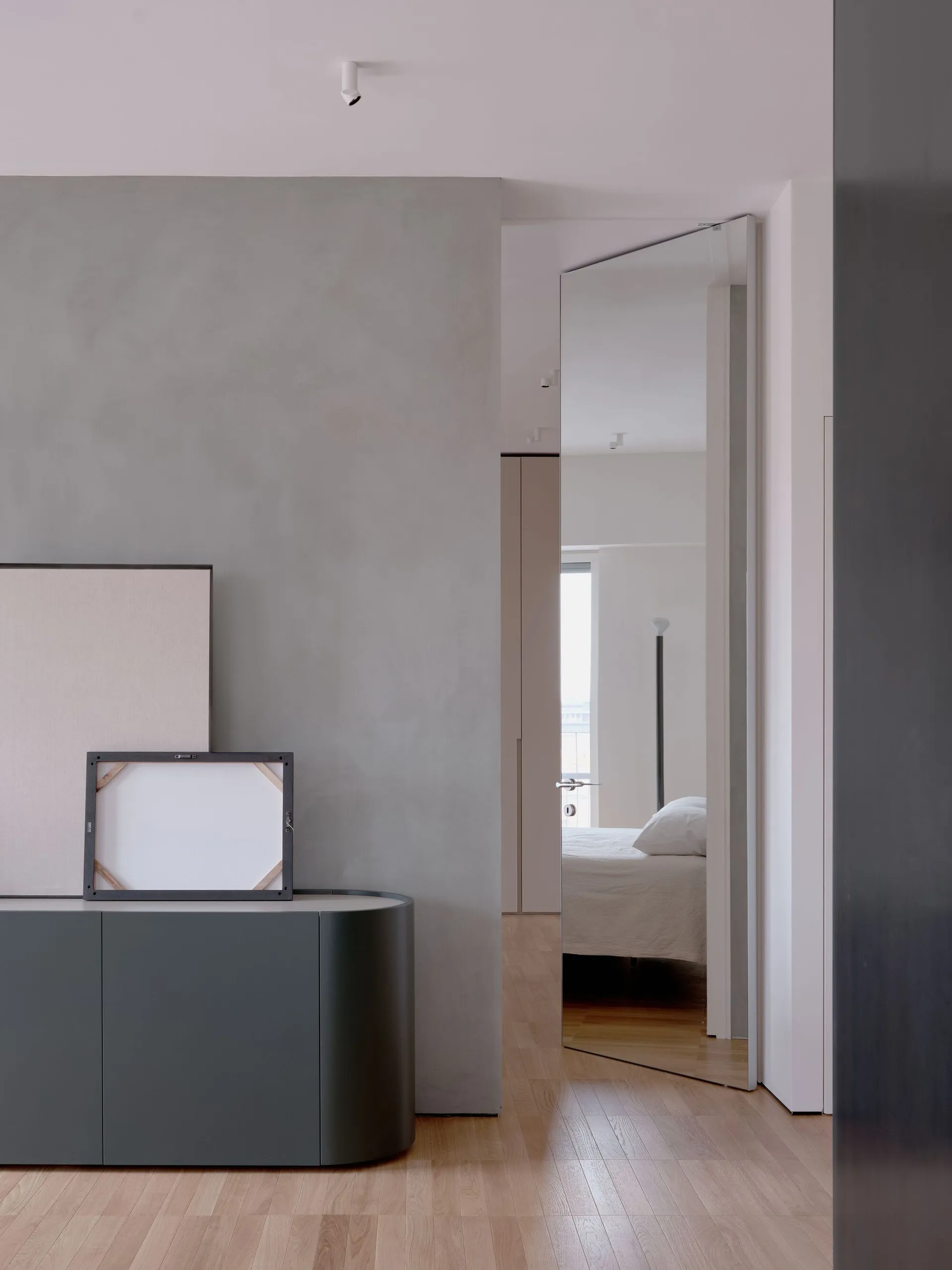 A modern minimalist bedroom with concrete walls, a wood floor, and a white bed