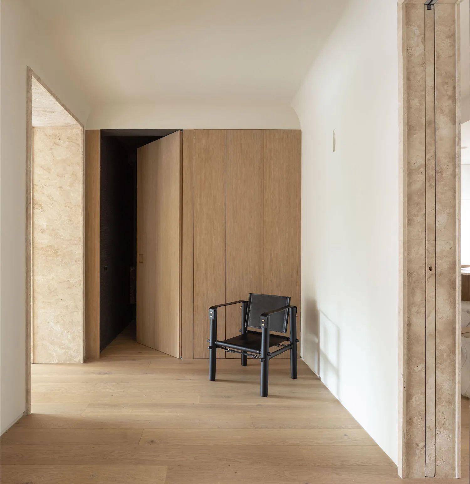 Modern minimalist interior with oak wood flooring, walls, and wardrobe, featuring a black chair.