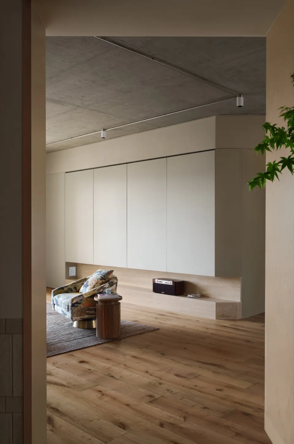 A minimalist living room featuring wood flooring, glass doors, and concrete walls.
