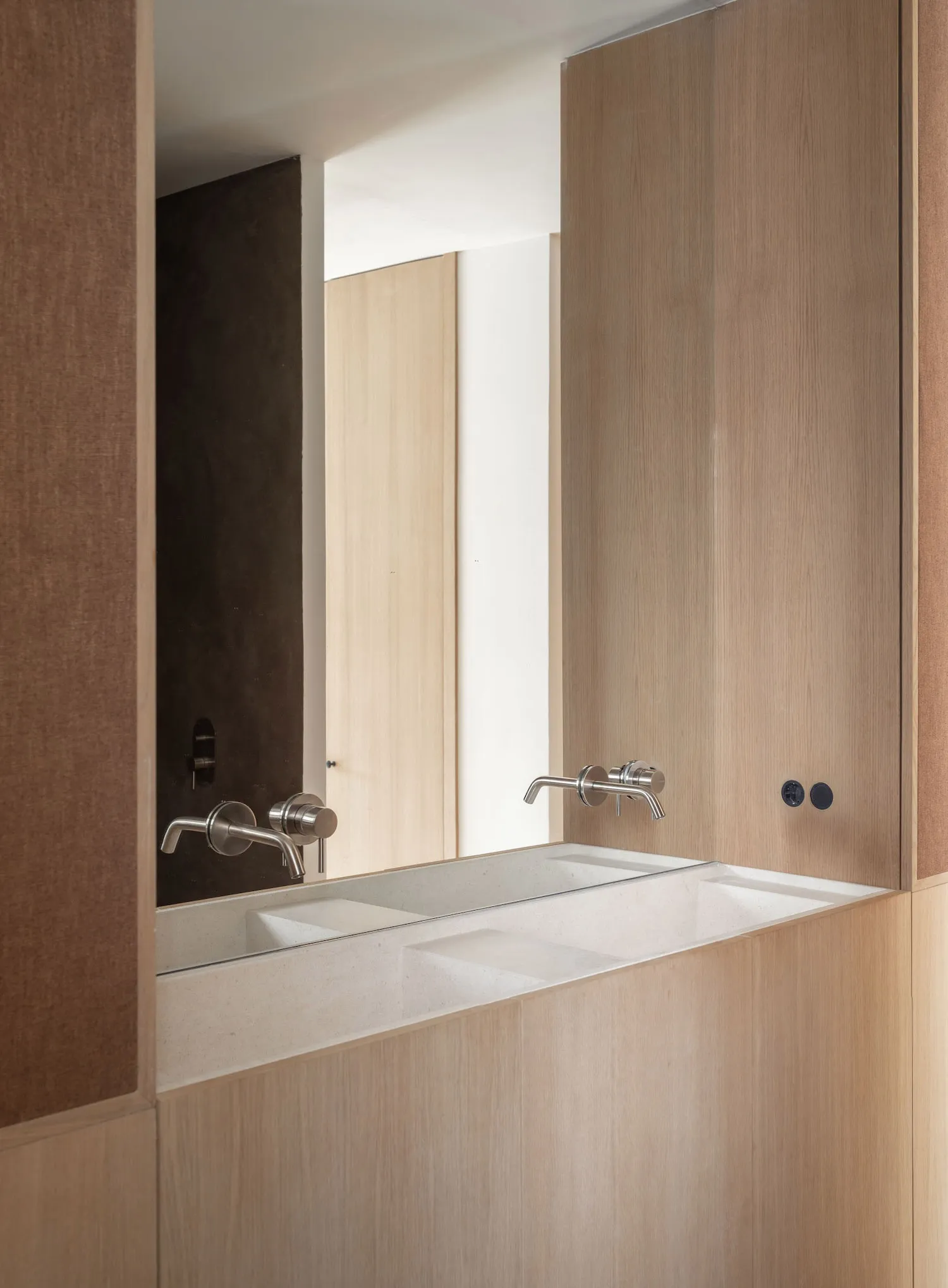 Modern minimalist bathroom with wooden fixtures and a long, rectangular sink with faucets.