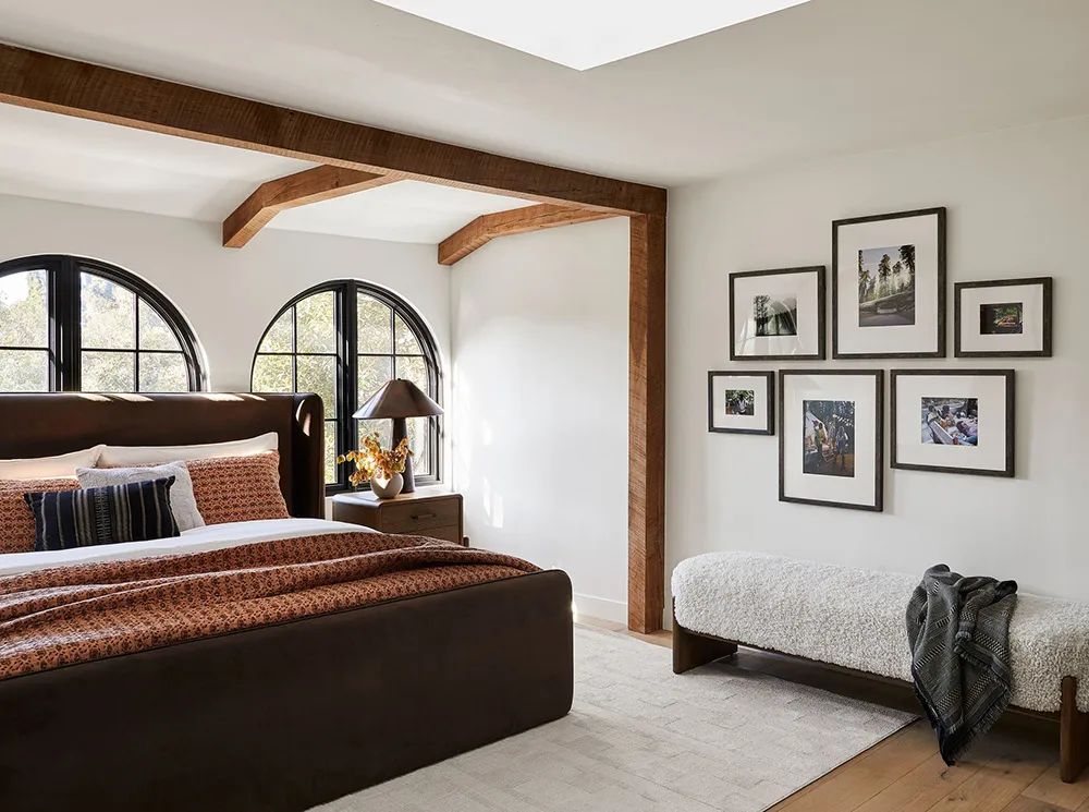 Modern bedroom showcasing a brown leather bed, wooden beams, and framed photographs on the wall.