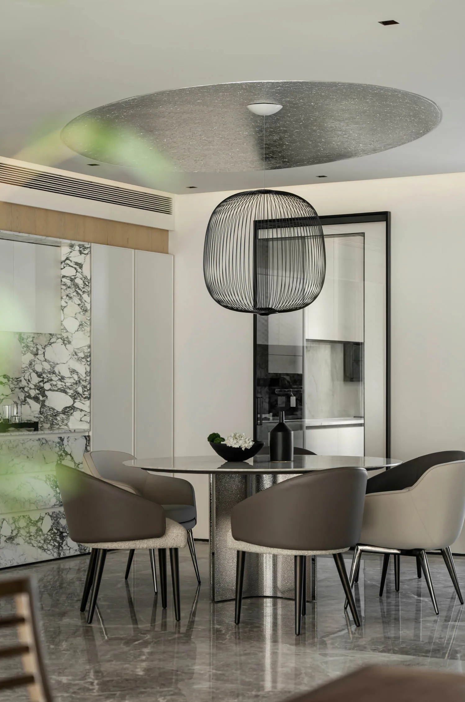Modern dining room with marble table, gray and beige leather chairs, and a round wire pendant light hanging from the ceiling.