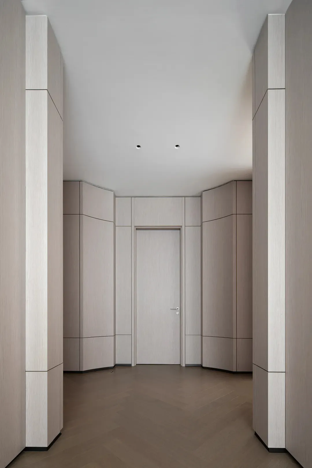 A modern corridor featuring grey-toned walls and flooring, with a closed door at the end.