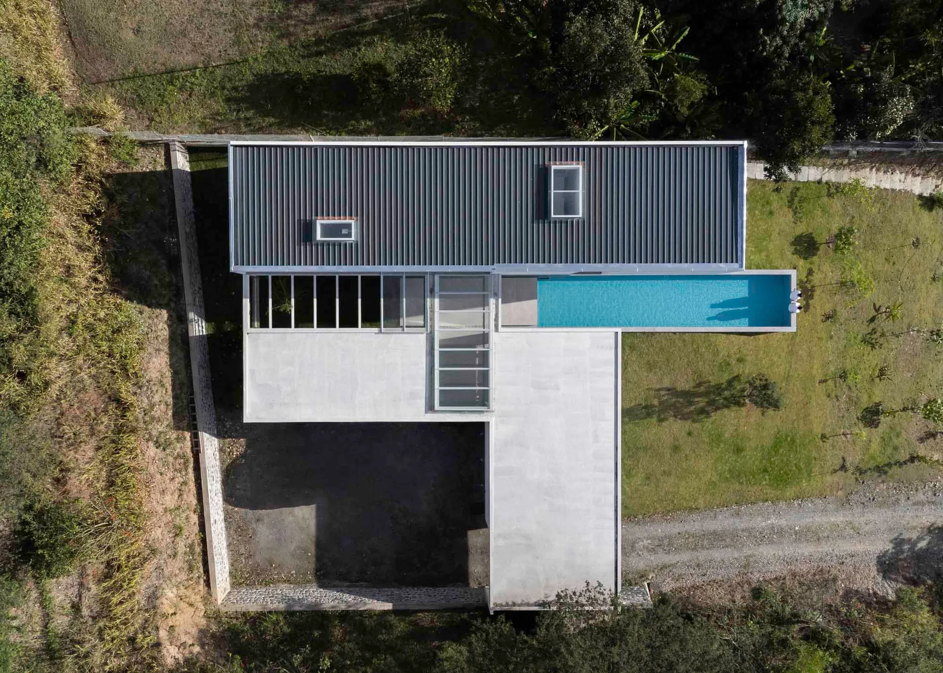 A modern house with a concrete floor plan, featuring a rooftop deck, large windows, and a swimming pool.