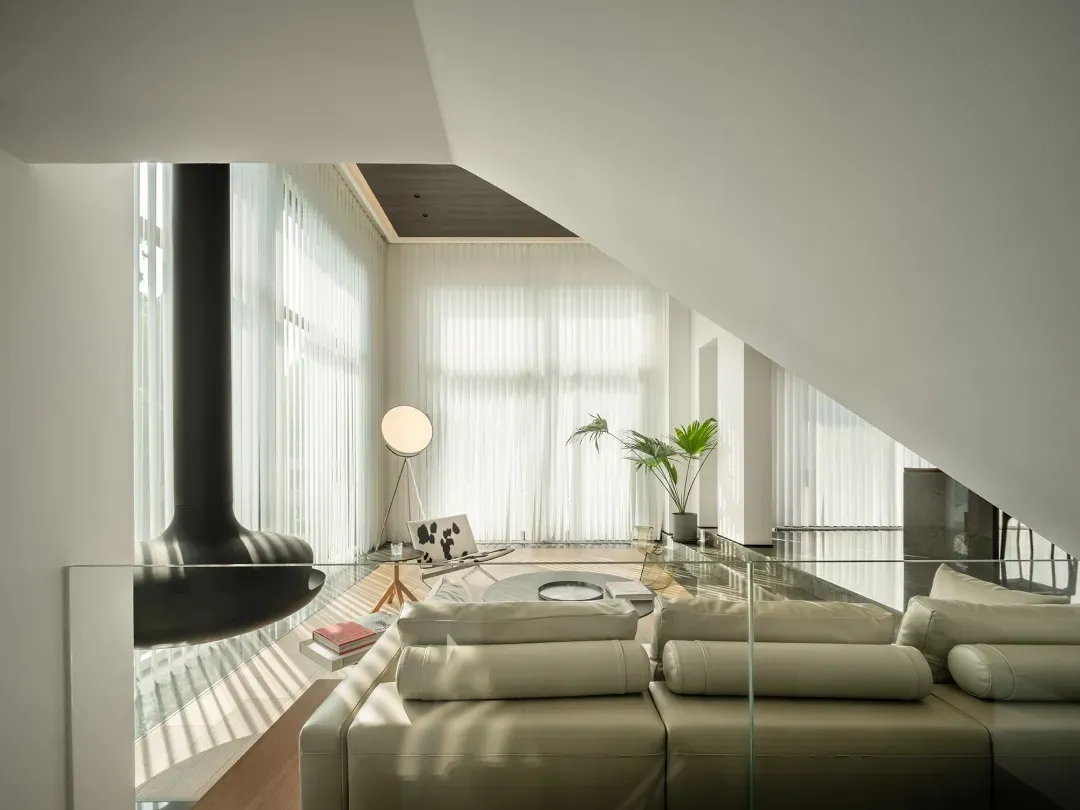 A modern living room featuring glass windows adorned with sheer white shades, a stylish leather couch, and a warm wooden floo