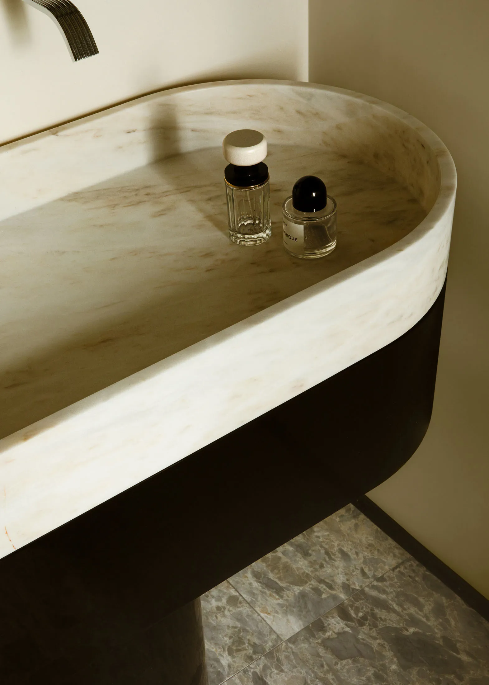 A modern bathroom counter made of marble with two small bottles on top.