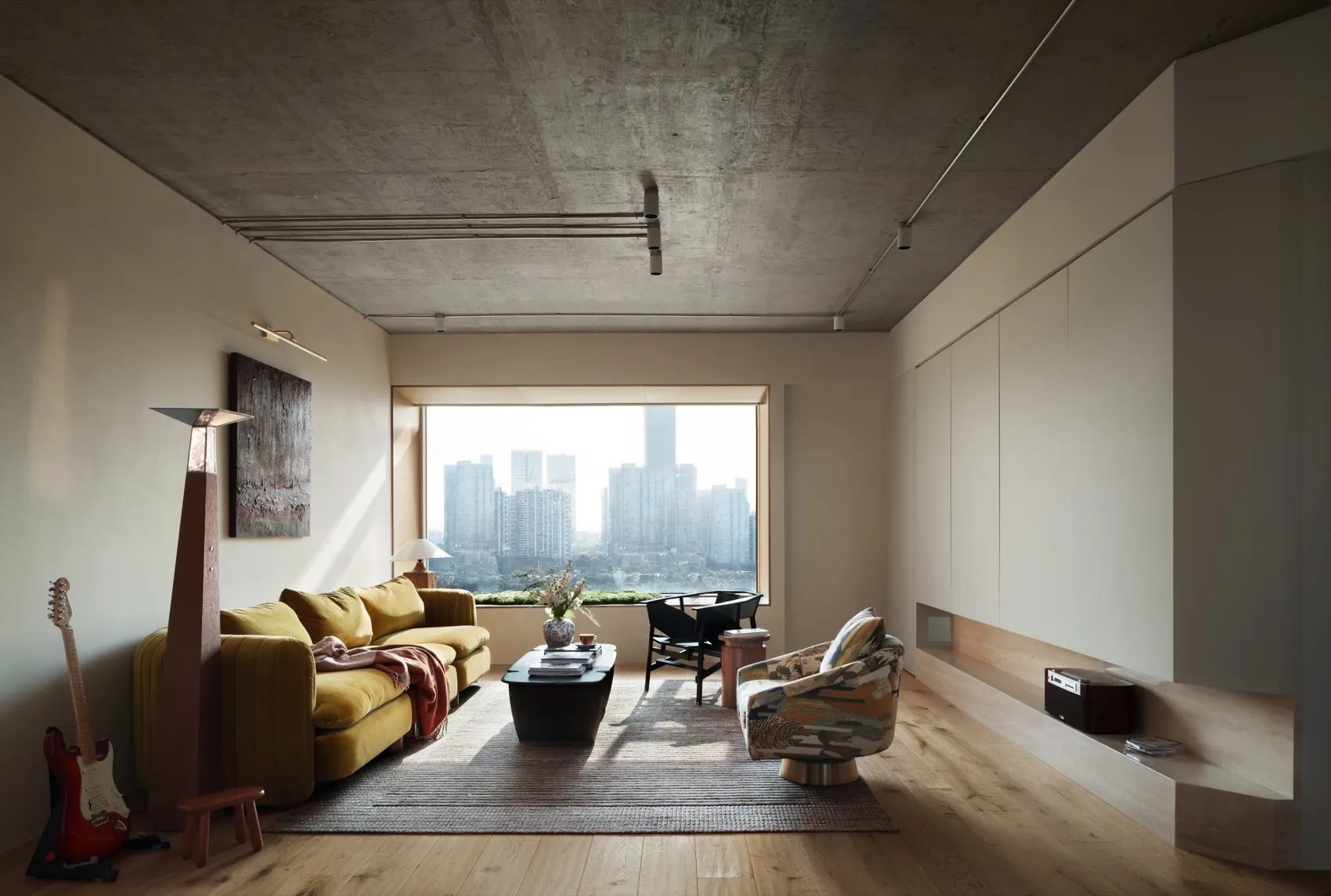 A modern minimalist living room featuring a yellow couch, a coffee table with a vase and a book, a guitar, and a view of a ci