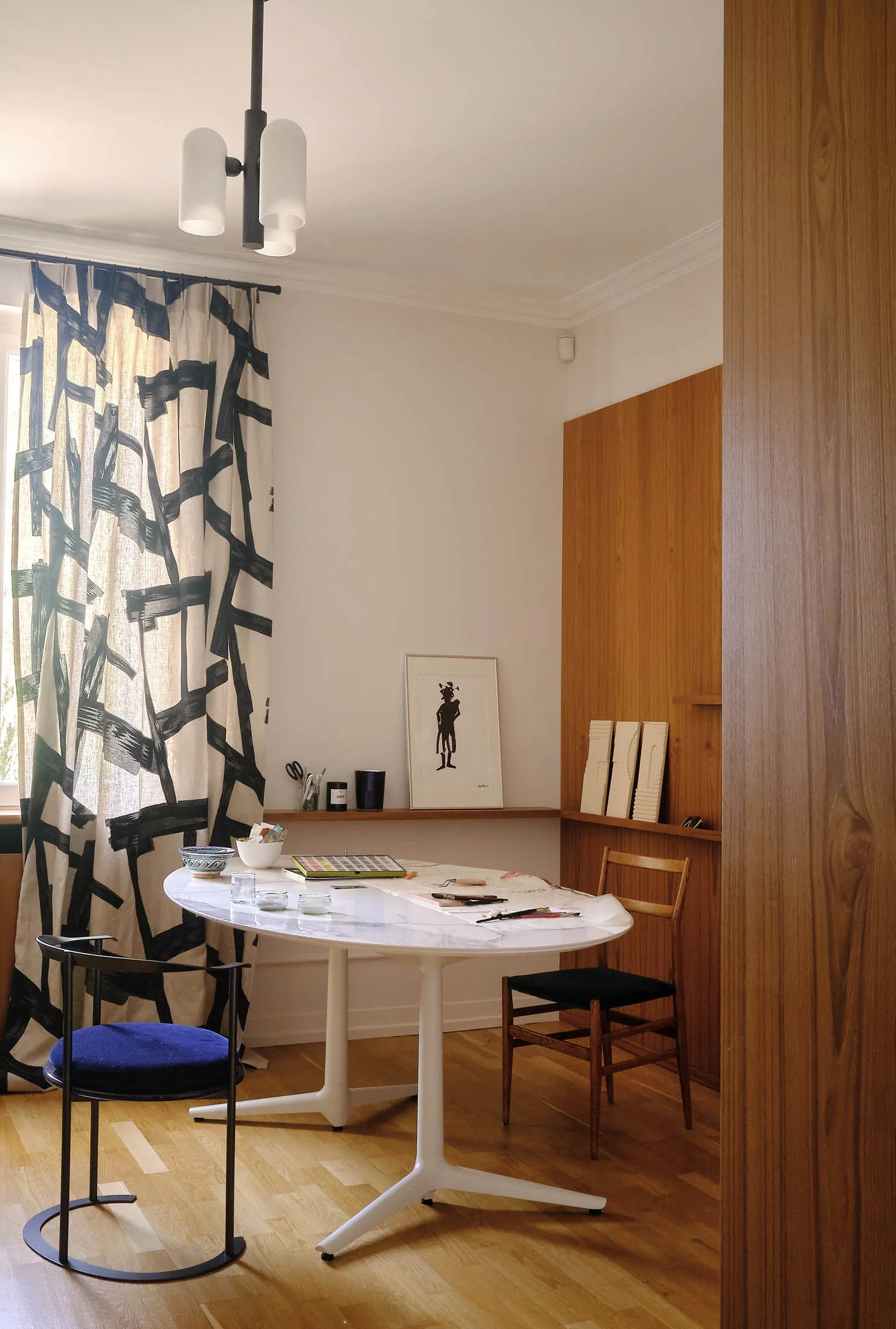 A modern minimalist kitchen featuring a white marble countertop, wood chairs, and black patterned curtains.