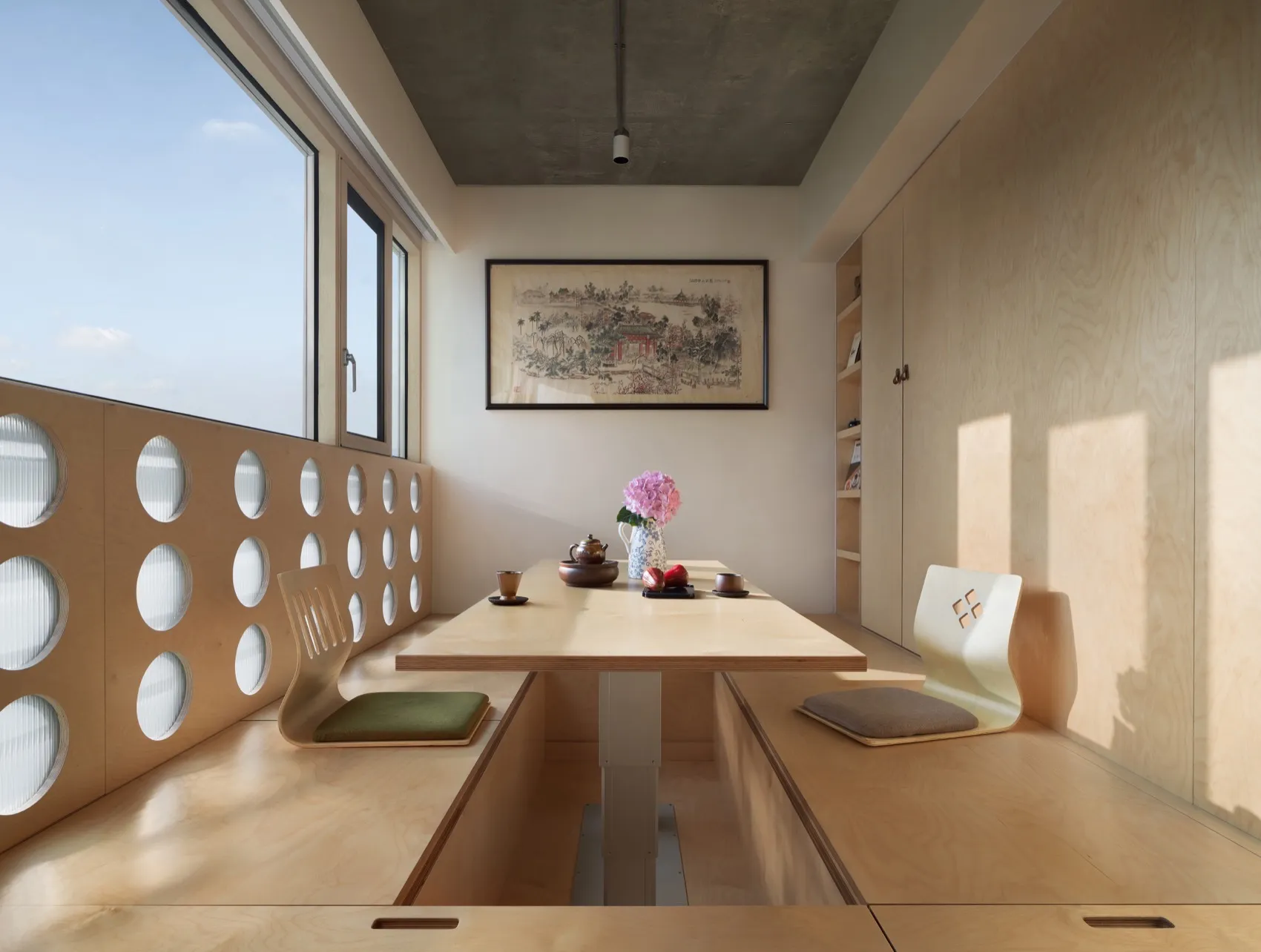 Modern minimalist dining room with a wooden floor and table, featuring a vase with flowers and a teapot, set against a backdr