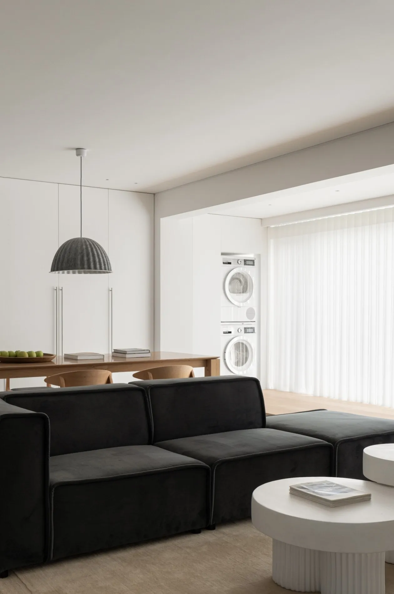 A modern living room featuring a black sofa on white flooring, with a wooden table in the background.