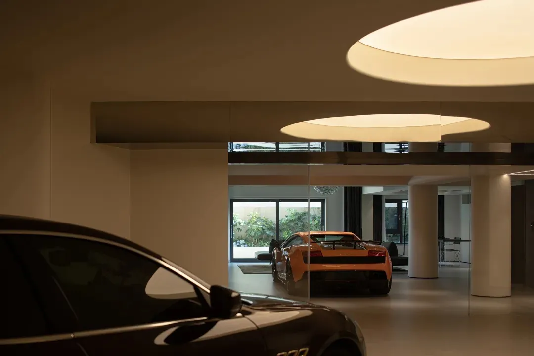 A modern garage with glass walls and floor, featuring high-end sports cars.