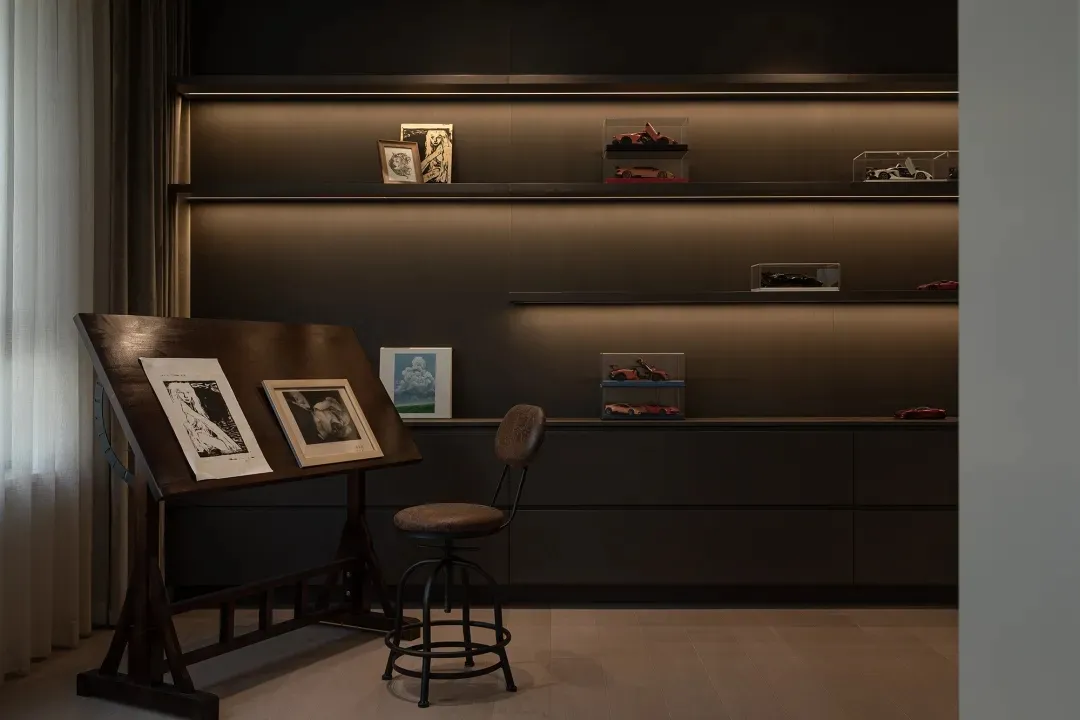 Modern home office with a wooden drafting table, framed artwork, and display shelves with model cars.