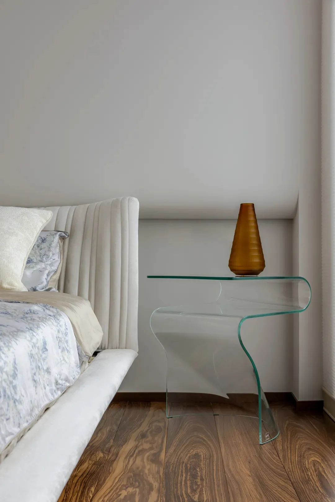 A modern bedroom interior featuring a glass nightstand with a unique curved shape.