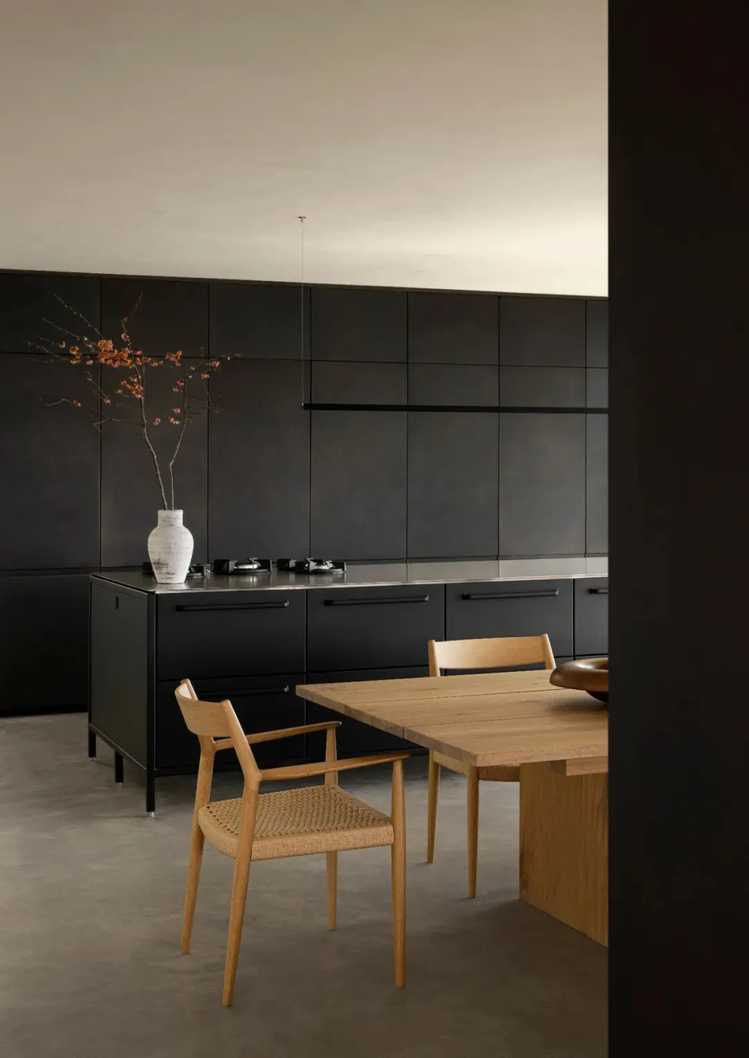 A modern kitchen with black panels and a wooden dining table.
