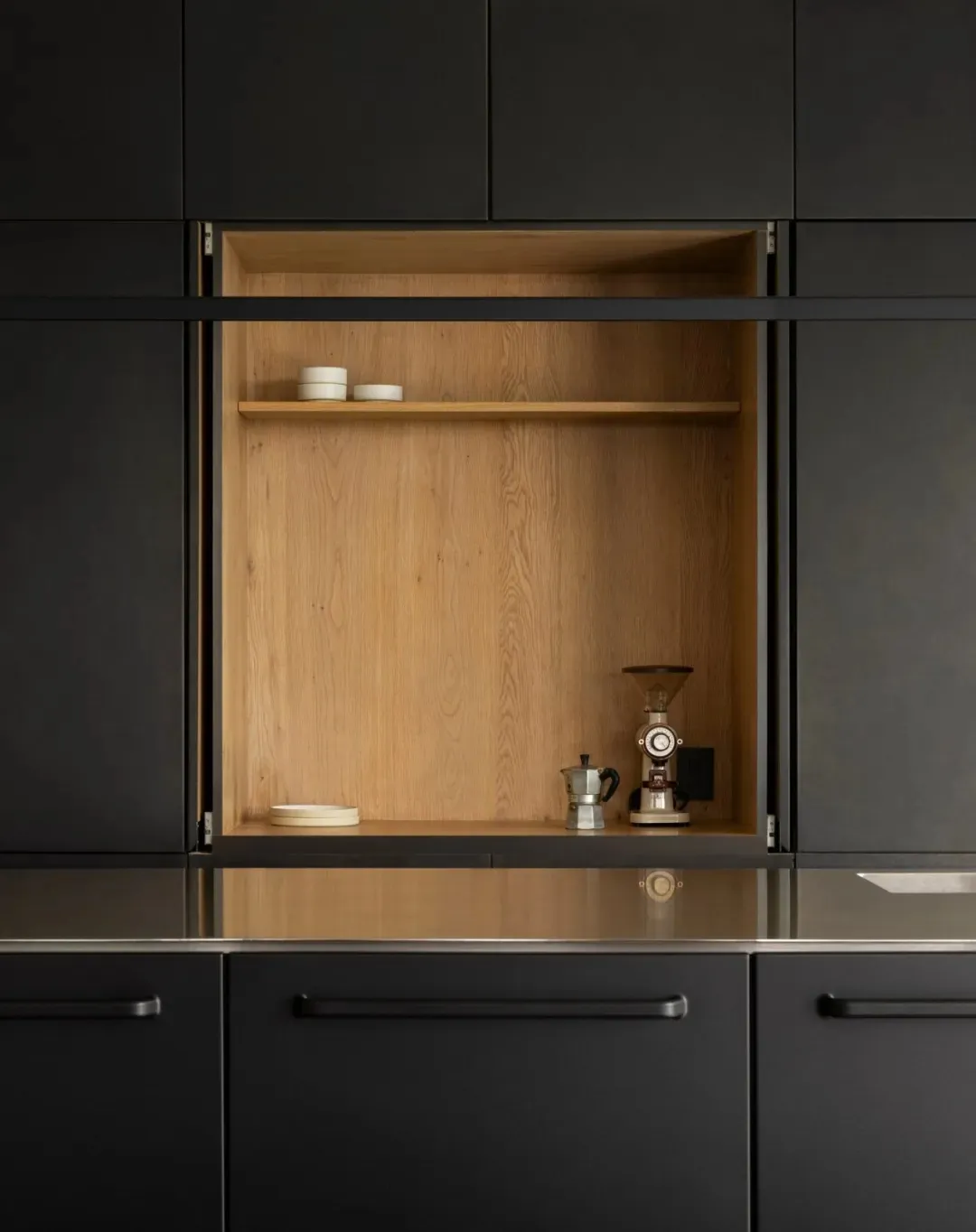 Black kitchen cabinets with a wooden storage unit containing a coffee grinder and a coffee maker.