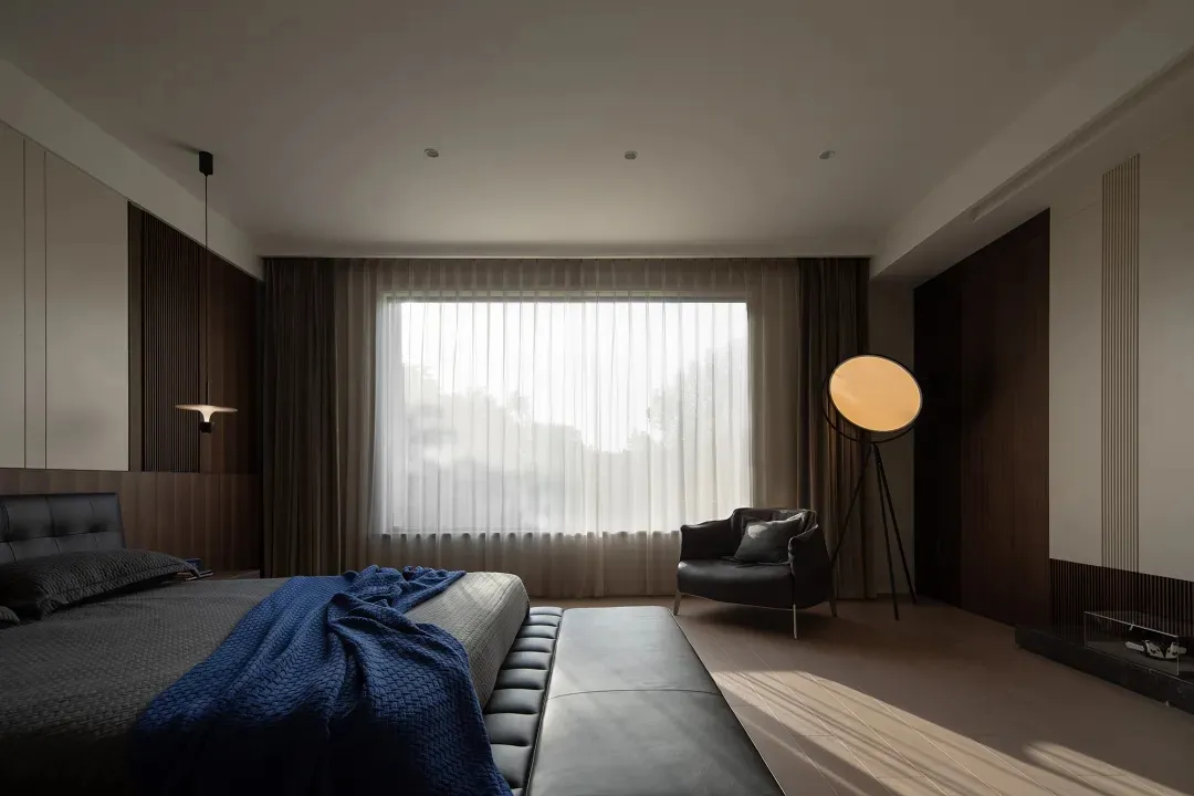 A modern bedroom featuring a bed with striped coverings, a textured wooden headboard, and a leather bench.