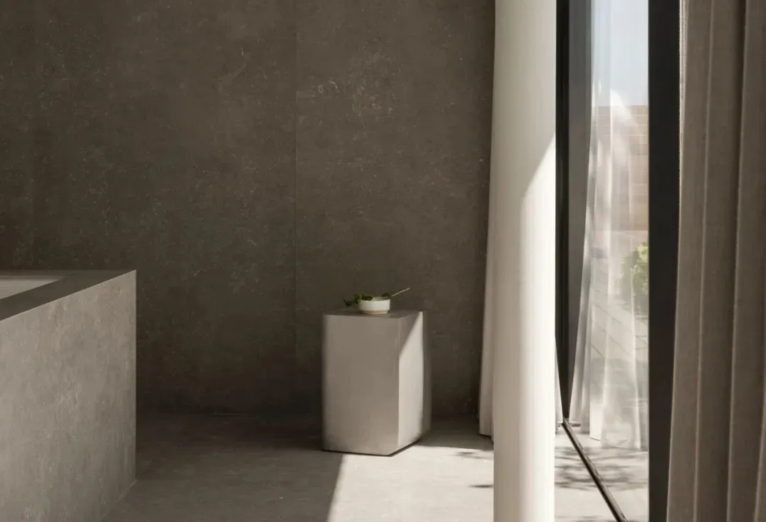 Modern minimalist bathroom featuring a concrete floor and walls, with a white pedestal and greenery.