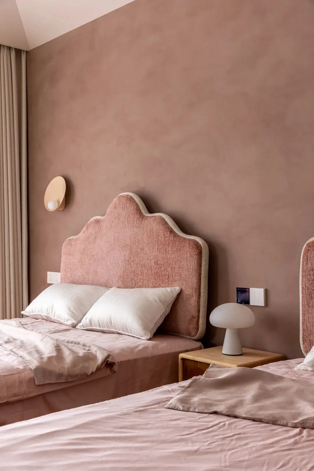 A minimalist bedroom with pink upholstered headboards and pink bedding on a bed with white pillows.