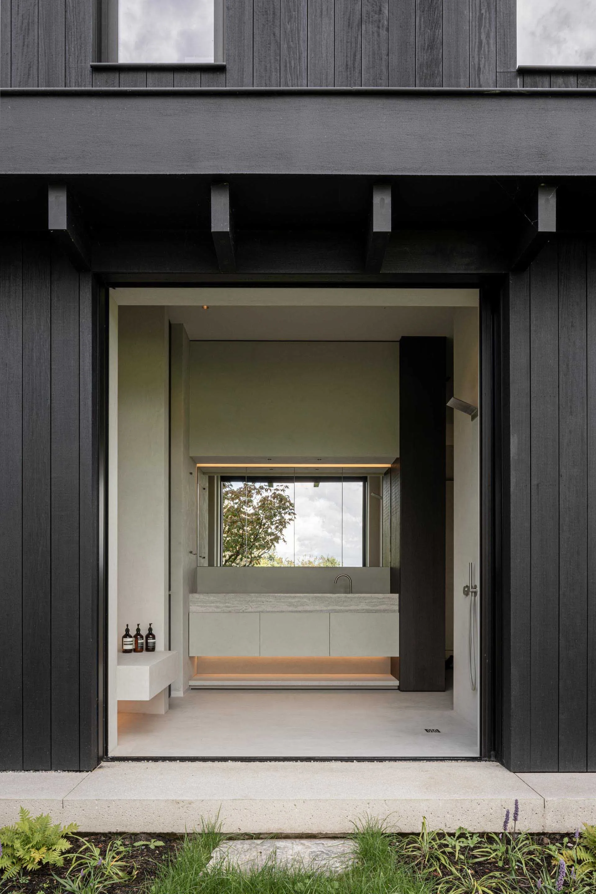 A modern, minimalist bathroom with concrete walls and floor, glass partition, and a sink with a large mirror.