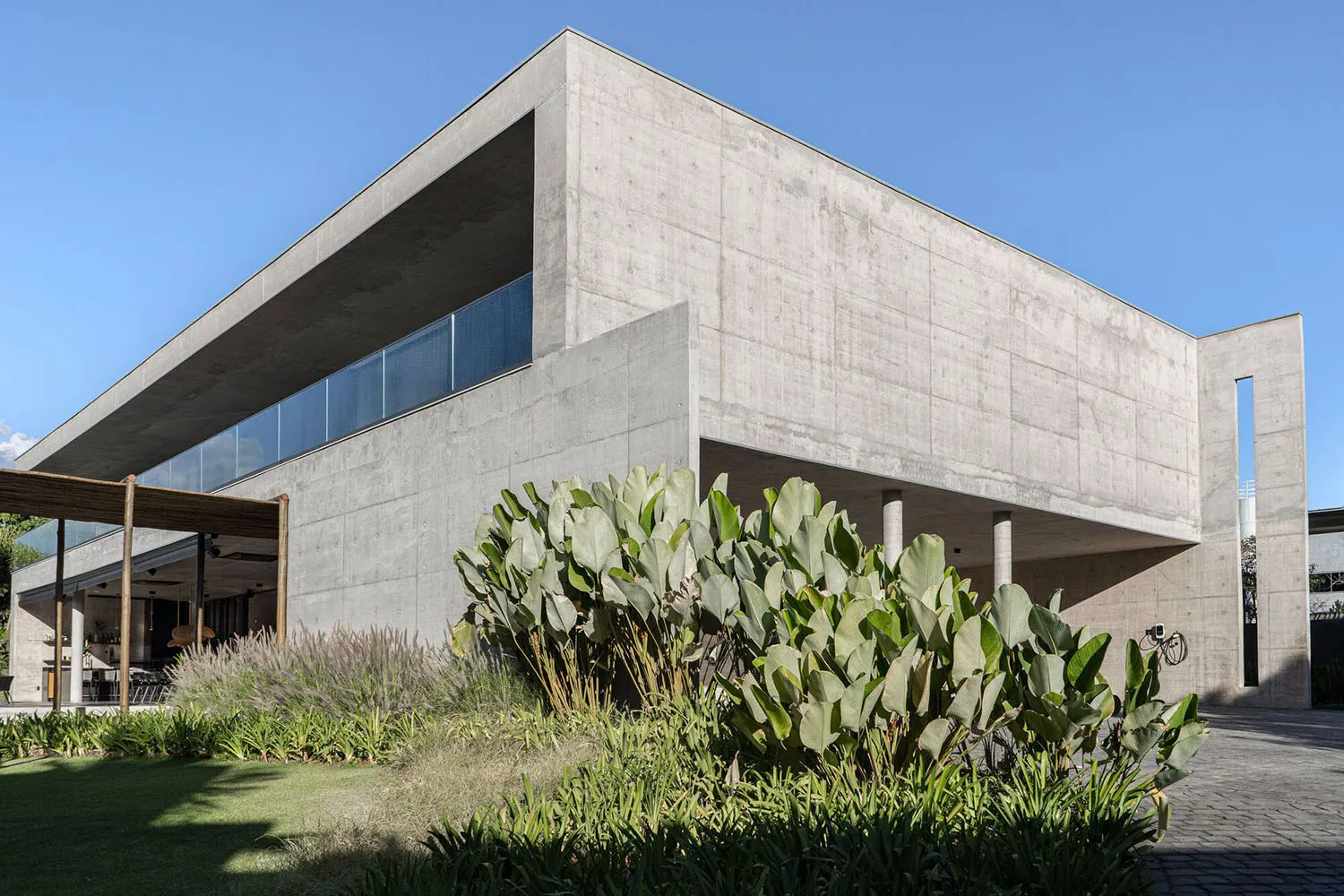 A modern concrete house exterior with a large glass window and a tropical garden.