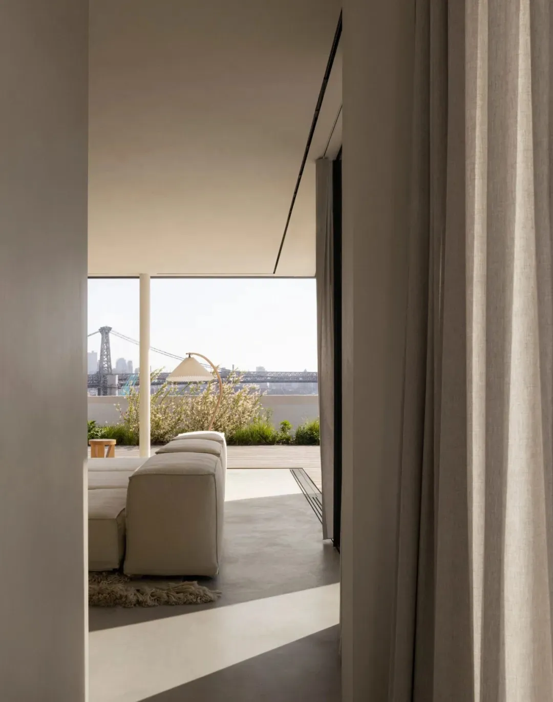 A modern, minimalist living space with concrete walls and floor, a white sectional sofa, and a floor lamp.