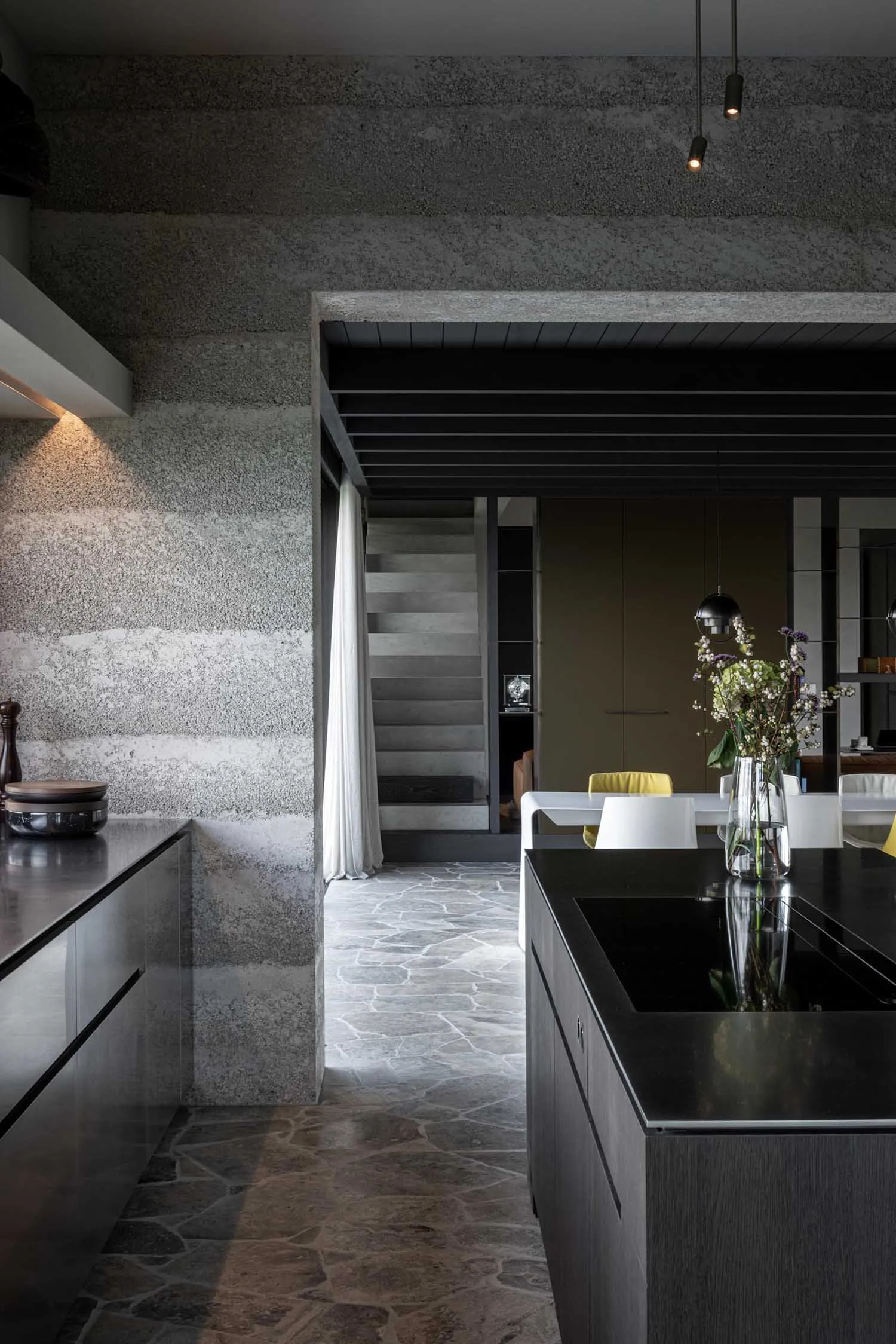 Modern kitchen with dark tones, featuring dark cabinets, a black countertop, and a textured gray wall.