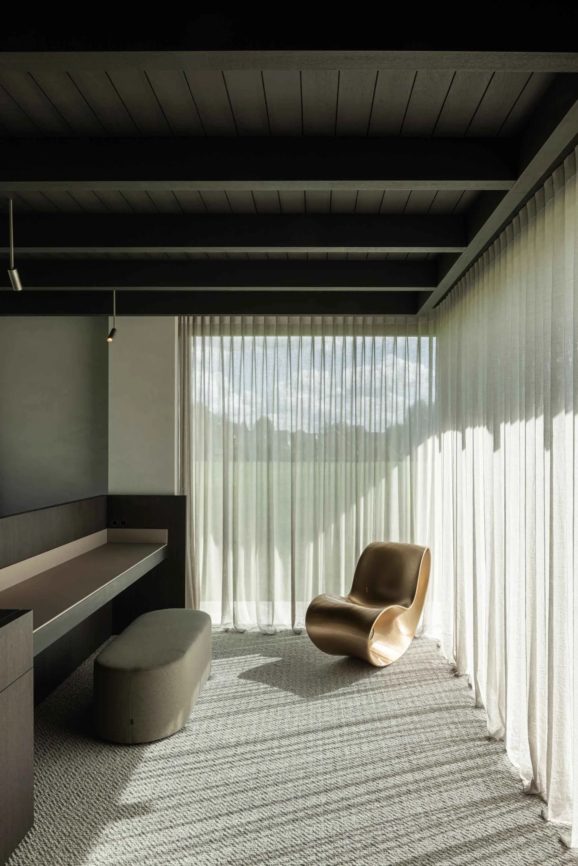 Modern living room featuring a metal chair, fabric window treatments, and a large window overlooking a serene outdoor view.