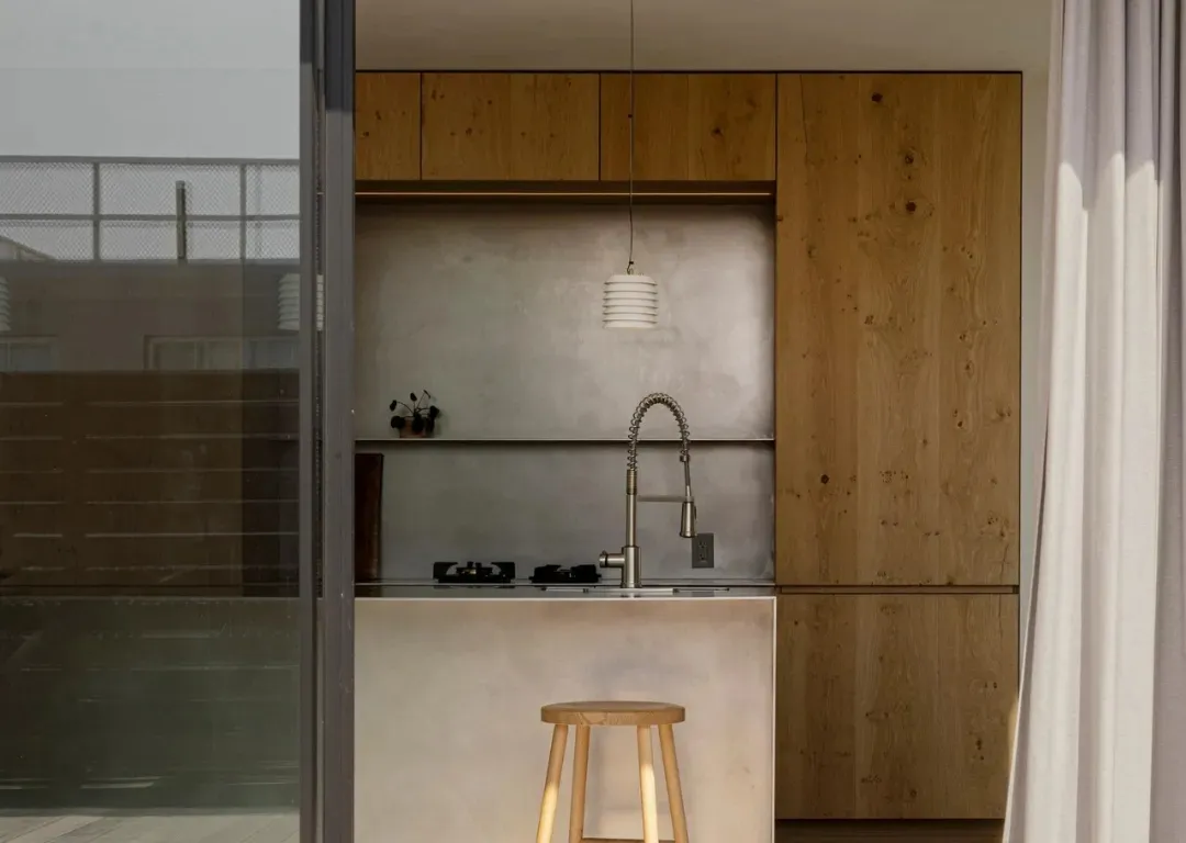 Modern minimalist kitchen with wood cabinets, concrete backsplash, and stainless steel sink.
