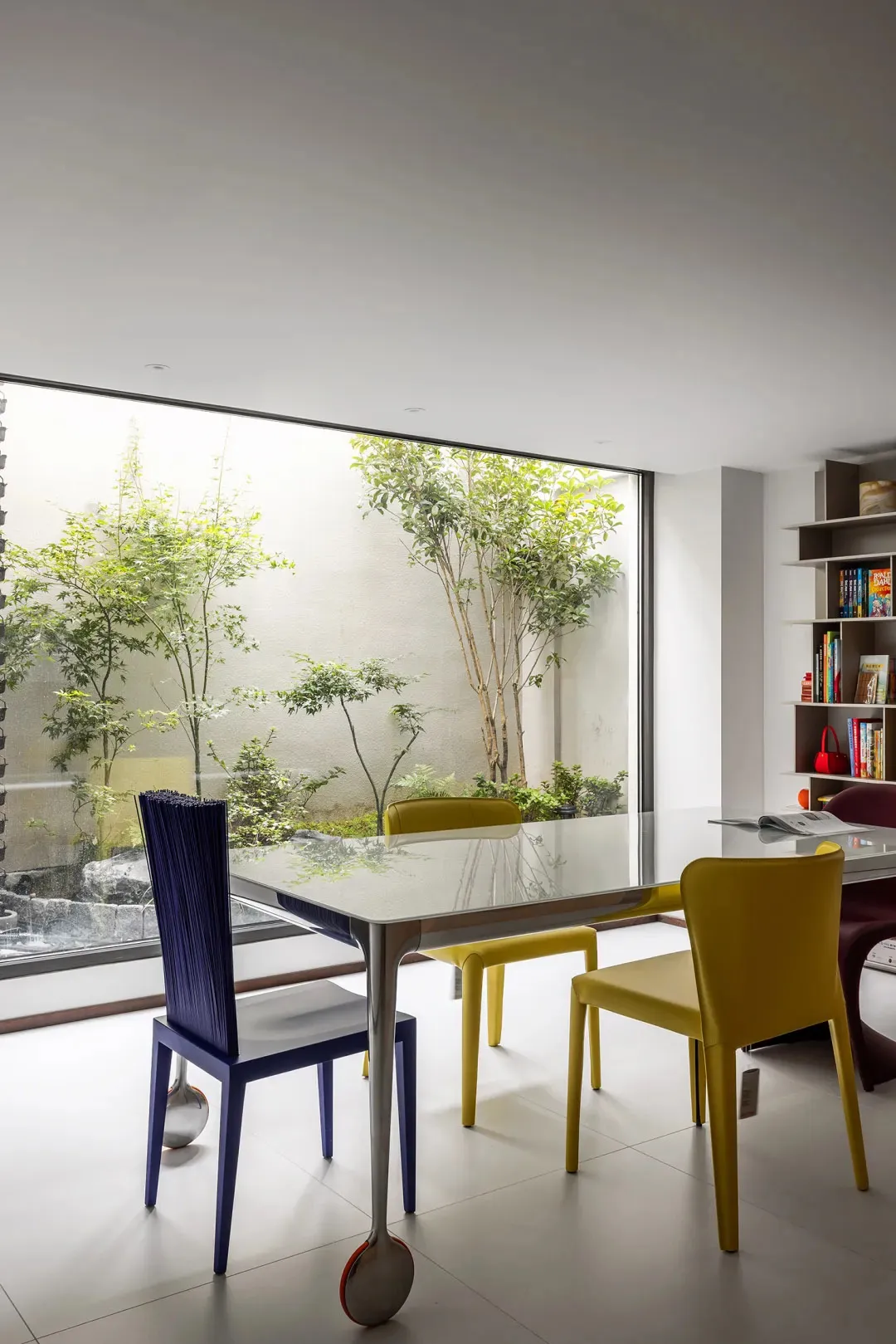 Contemporary dining room with glass table, yellow chairs, and indoor garden.