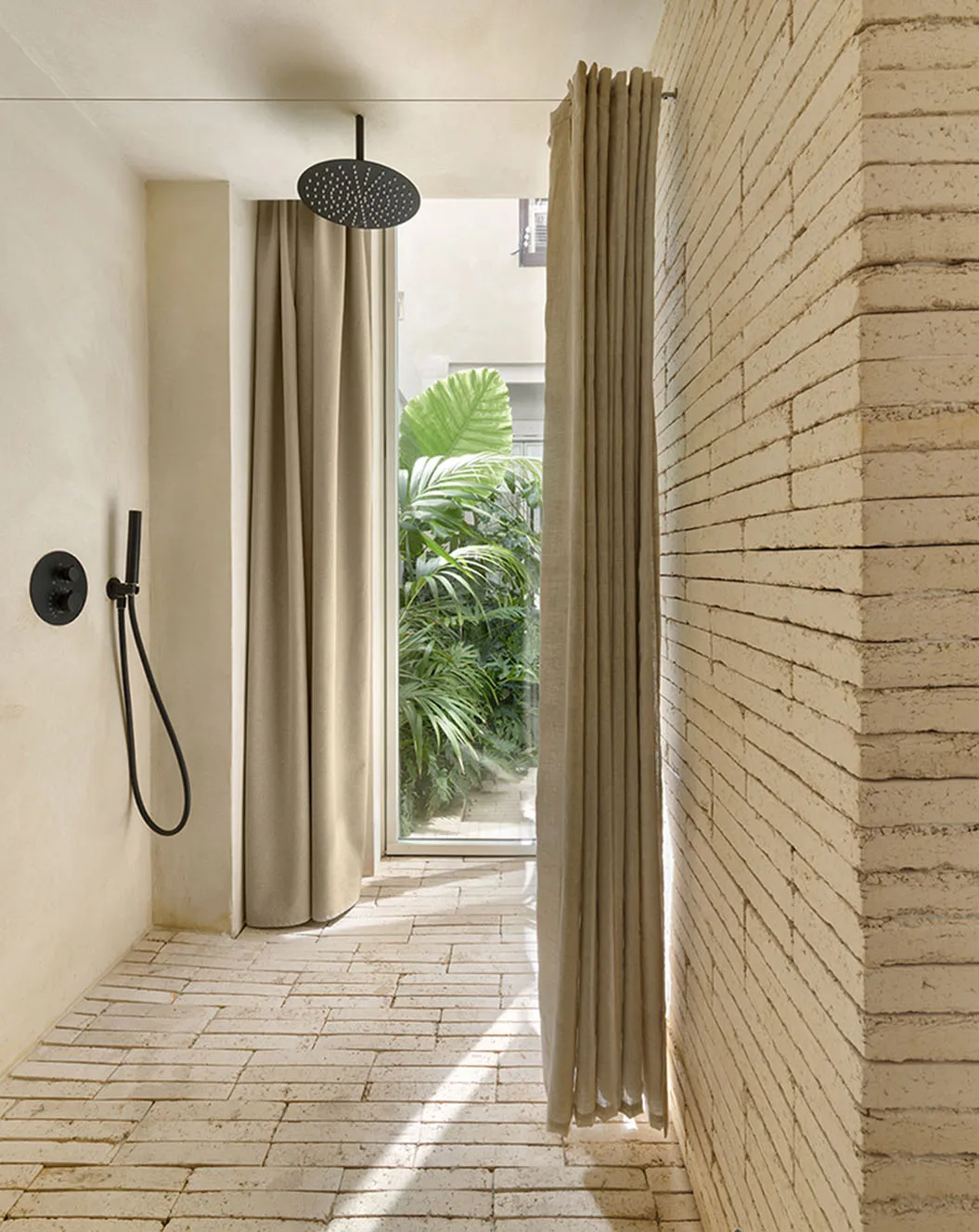Minimalist outdoor shower area with sandstone brick walls and concrete floor.