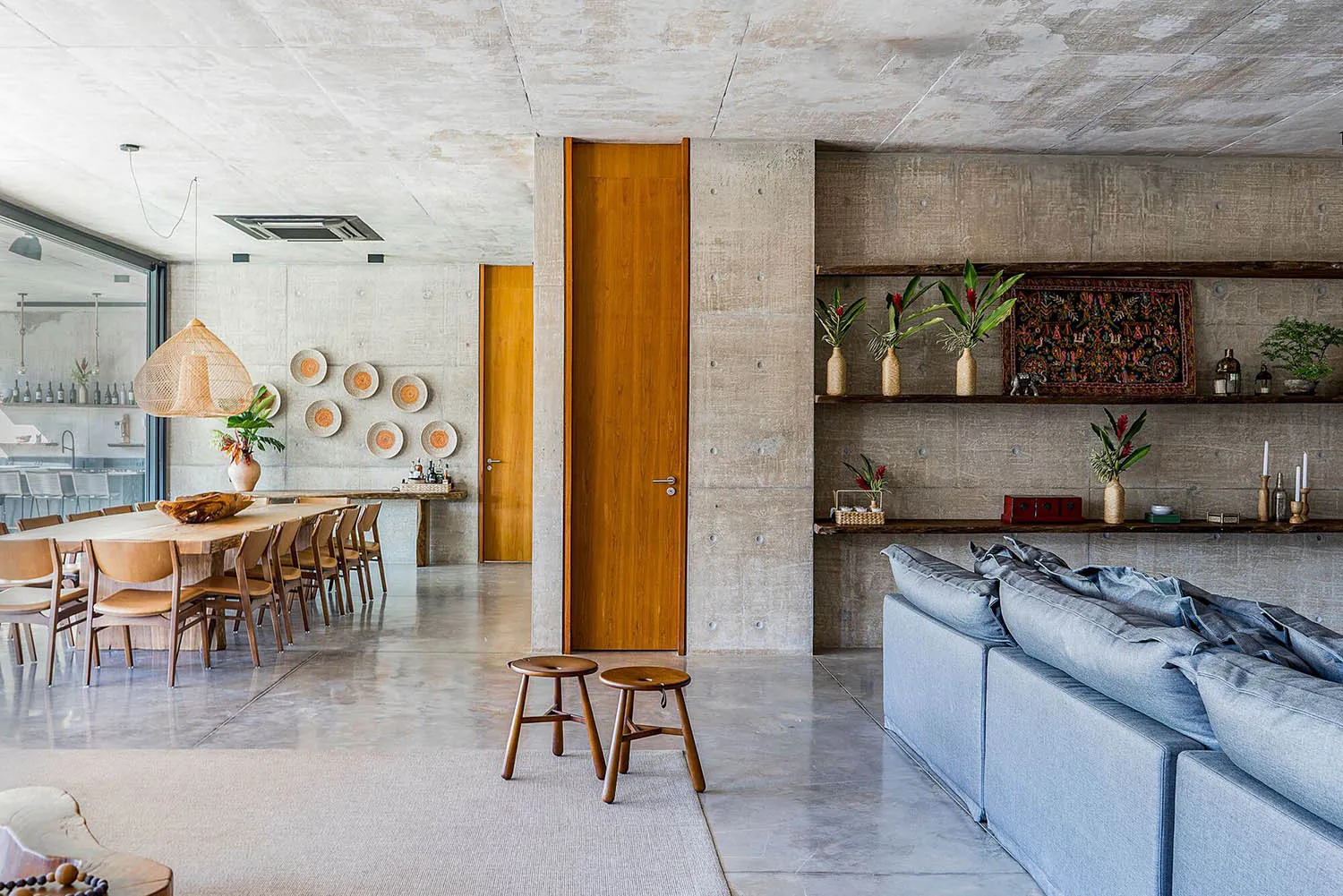 A modern interior design featuring a living and dining room with concrete walls, wooden doors, and a grey sofa.