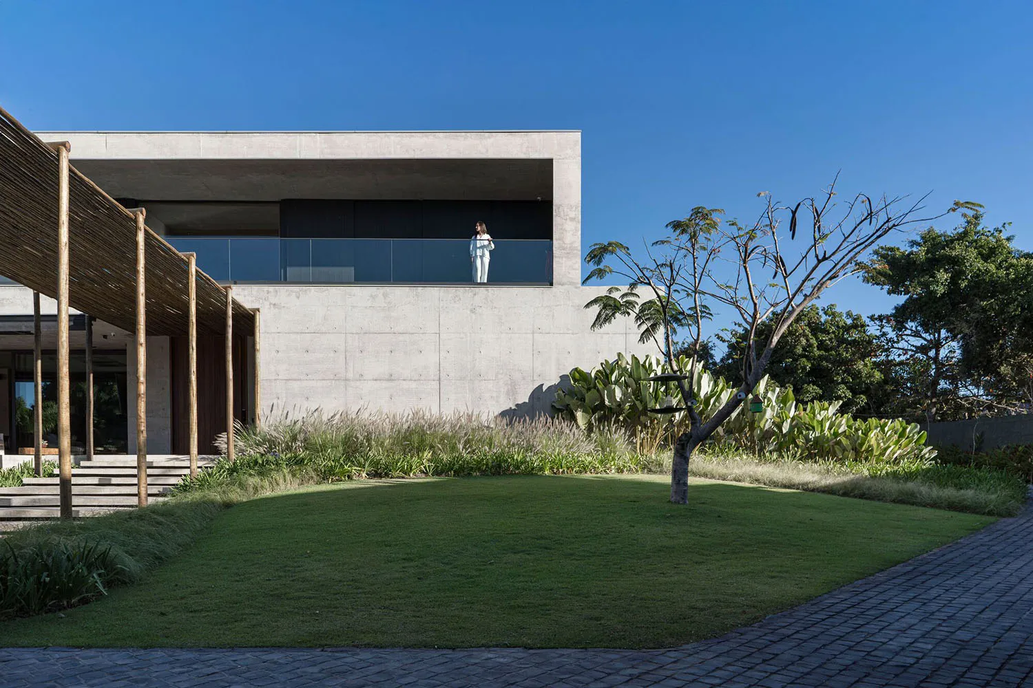 A modern house with a concrete exterior featuring a large glass balcony and greenery.
