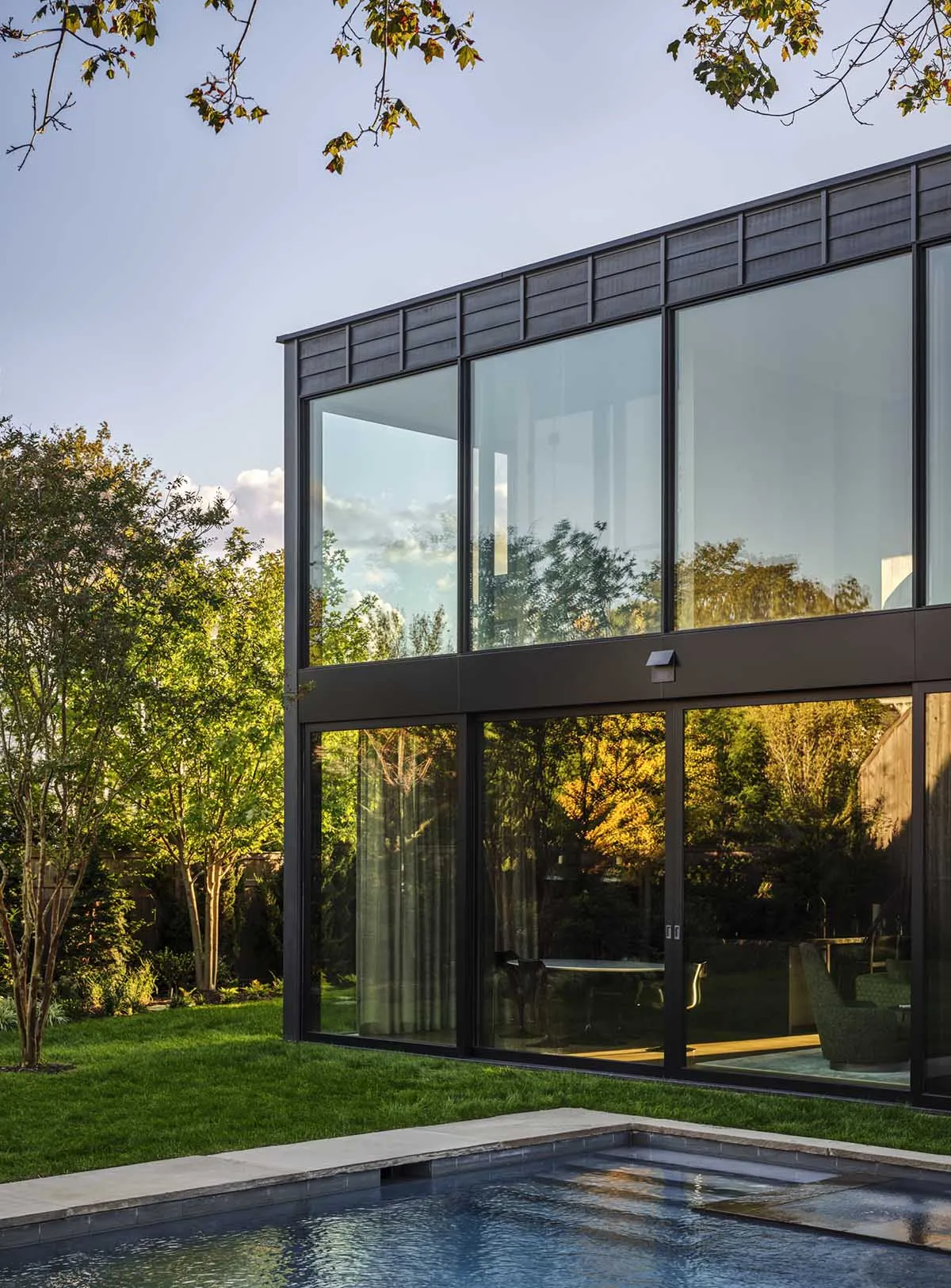 Modern house with large glass windows and a concrete base featuring a pool.