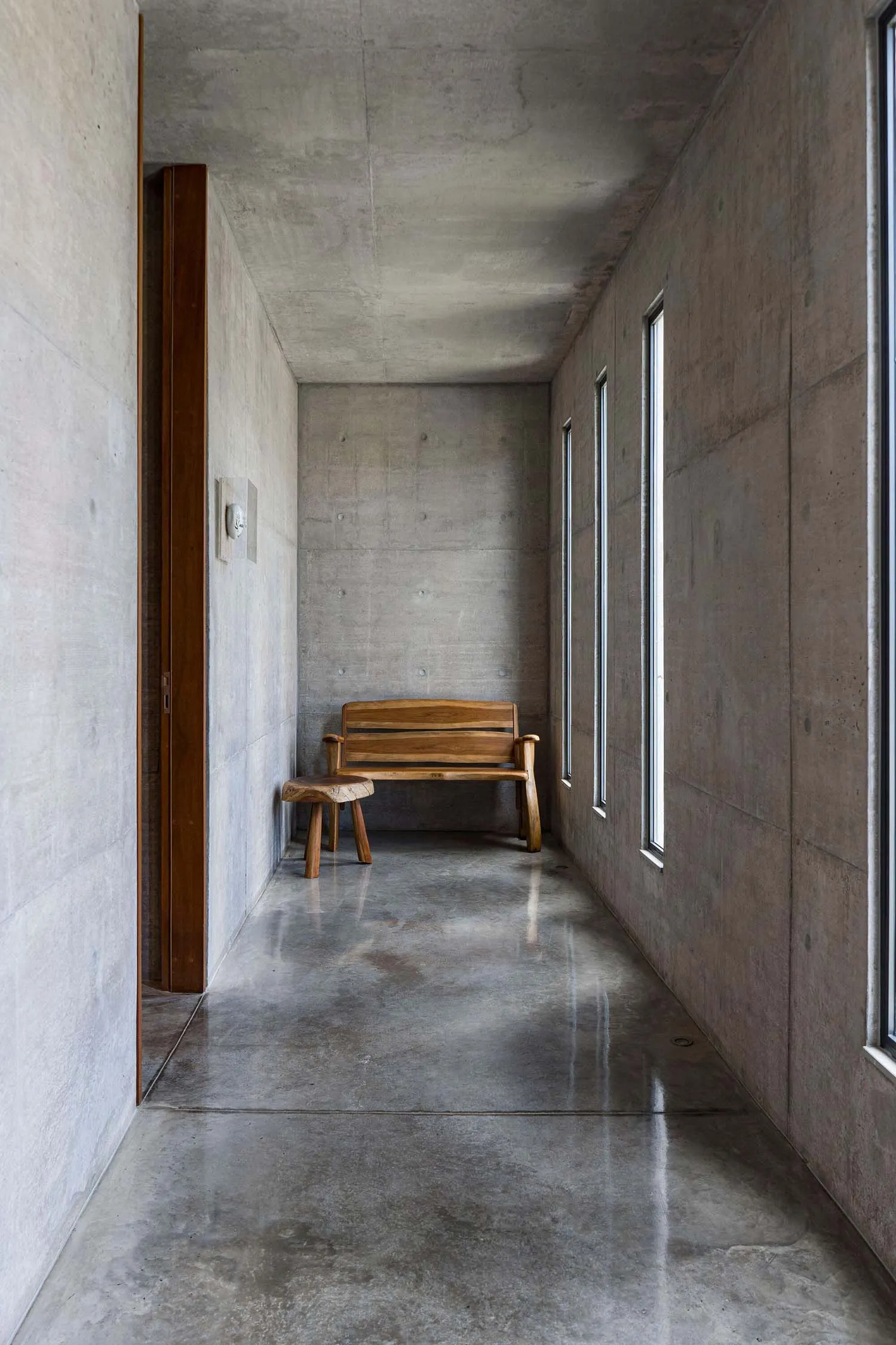 A minimalist, modern interior space featuring a concrete floor and walls, with a wooden bench in the center.