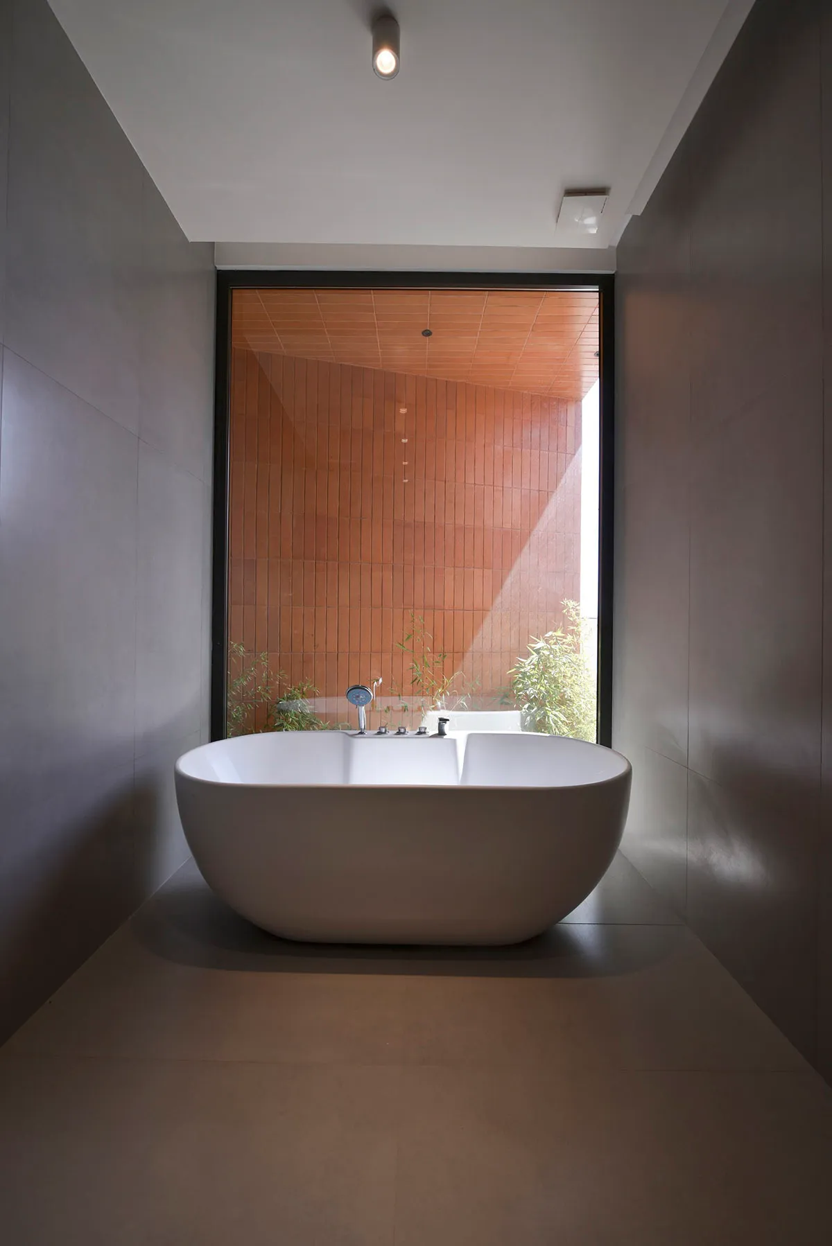 Modern minimalist bathroom with a white freestanding bathtub, ceramic tiles, and a large window showing greenery.
