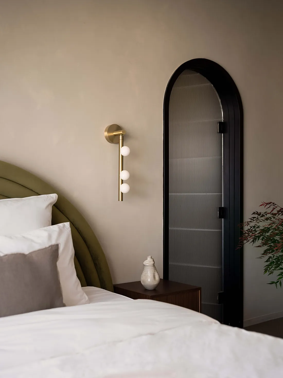 A modern bedroom with a fabric headboard, glass sconce, and white bed.
