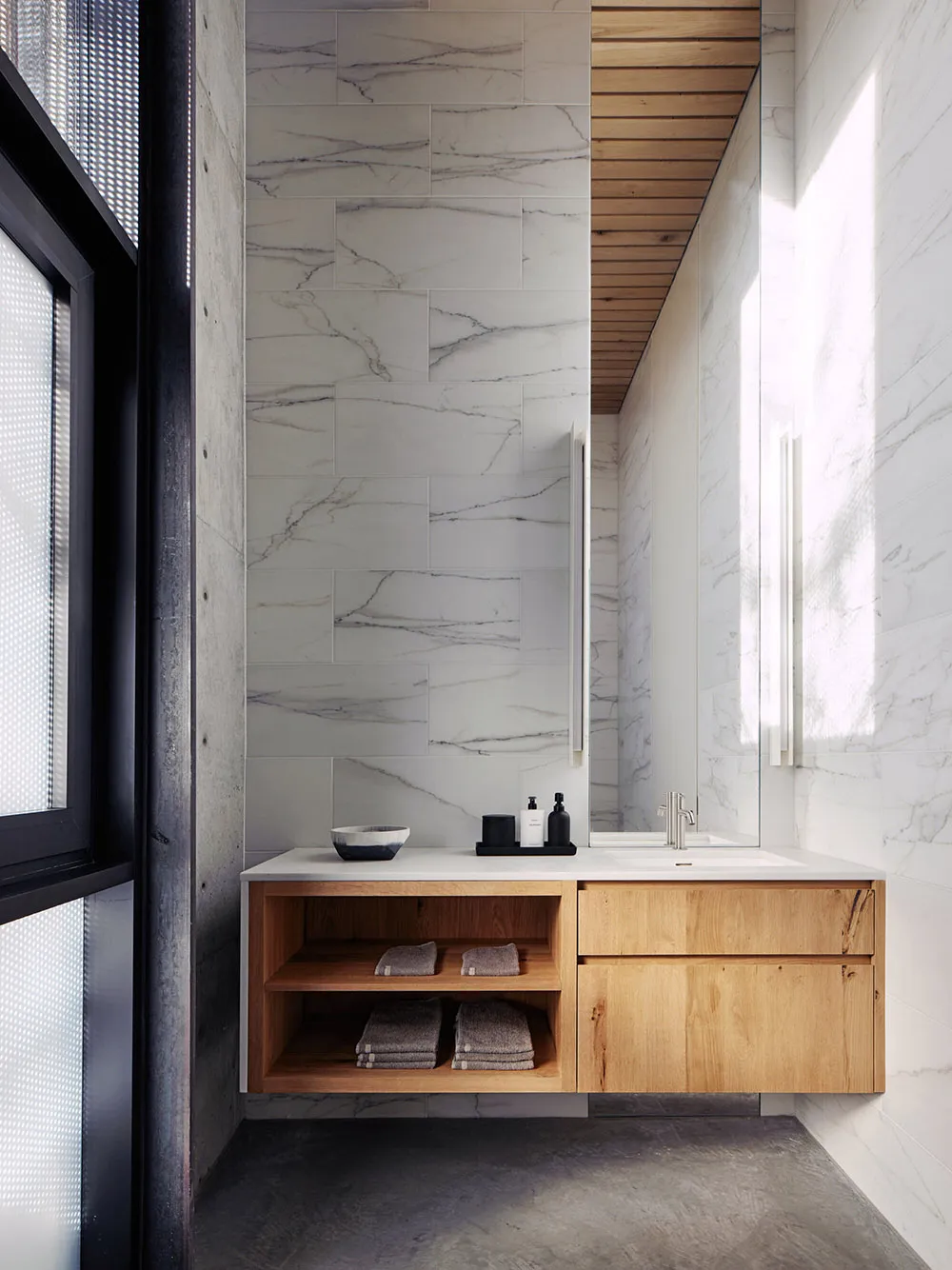 Modern minimalist bathroom featuring marble walls and a wooden vanity.