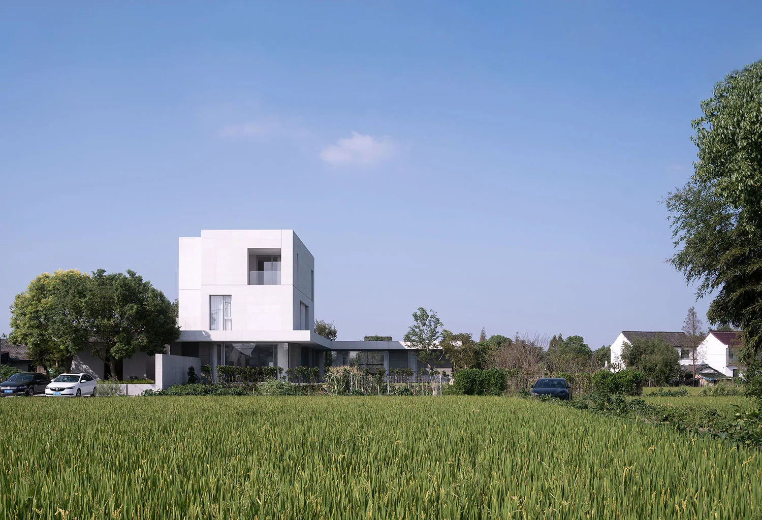 Modern white concrete residential home exterior with green grass and trees in the foreground.