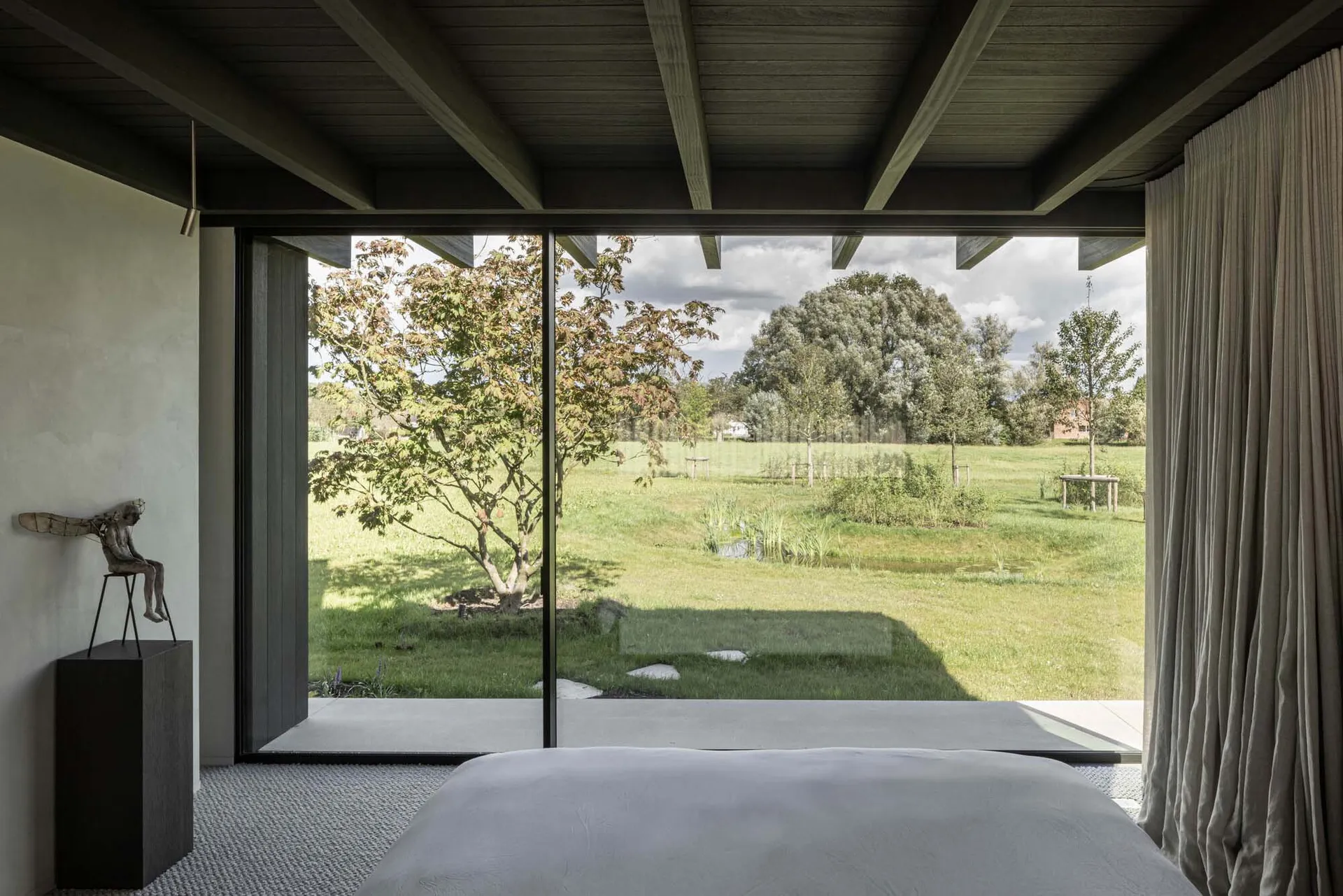 A minimalist bedroom with wood elements and a view of greenery through a large window.
